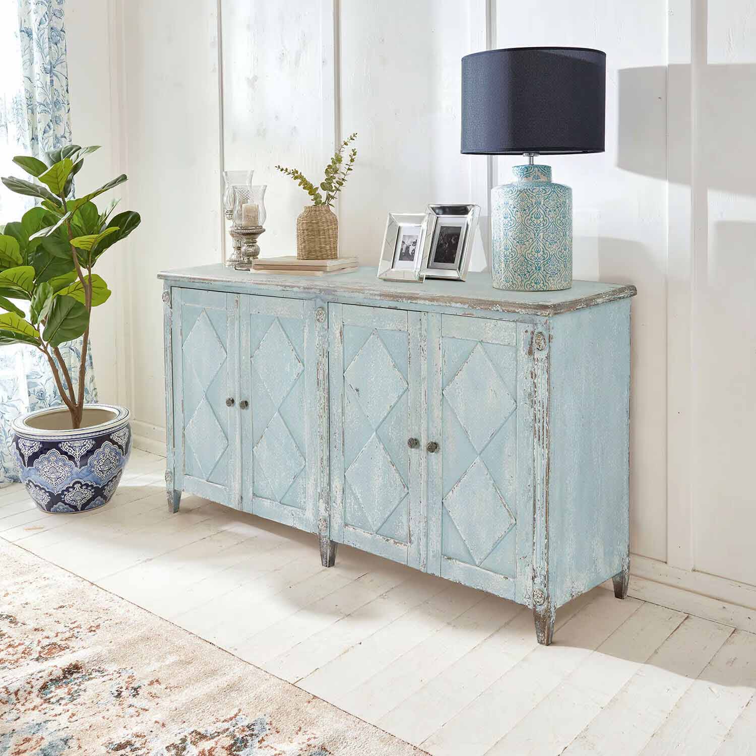 Hellblauer Holzschrank im Vintage-Stil mit Gebrauchsspuren, dekoriert mit Lampe und Pflanze im hellen Raum