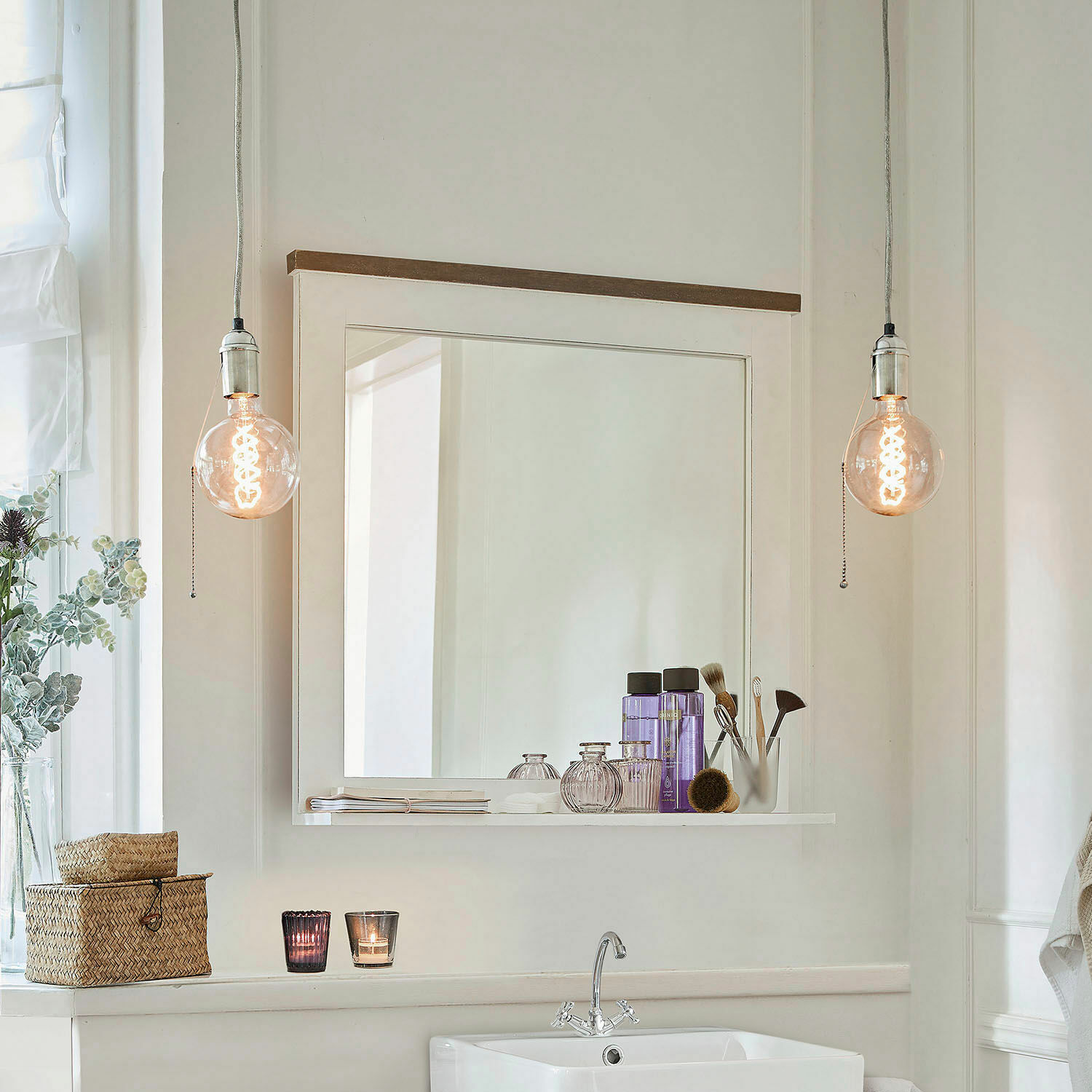 Badezimmer mit weißem Waschbecken, Spiegel mit Ablage und hängenden Vintage-Glühbirnen
