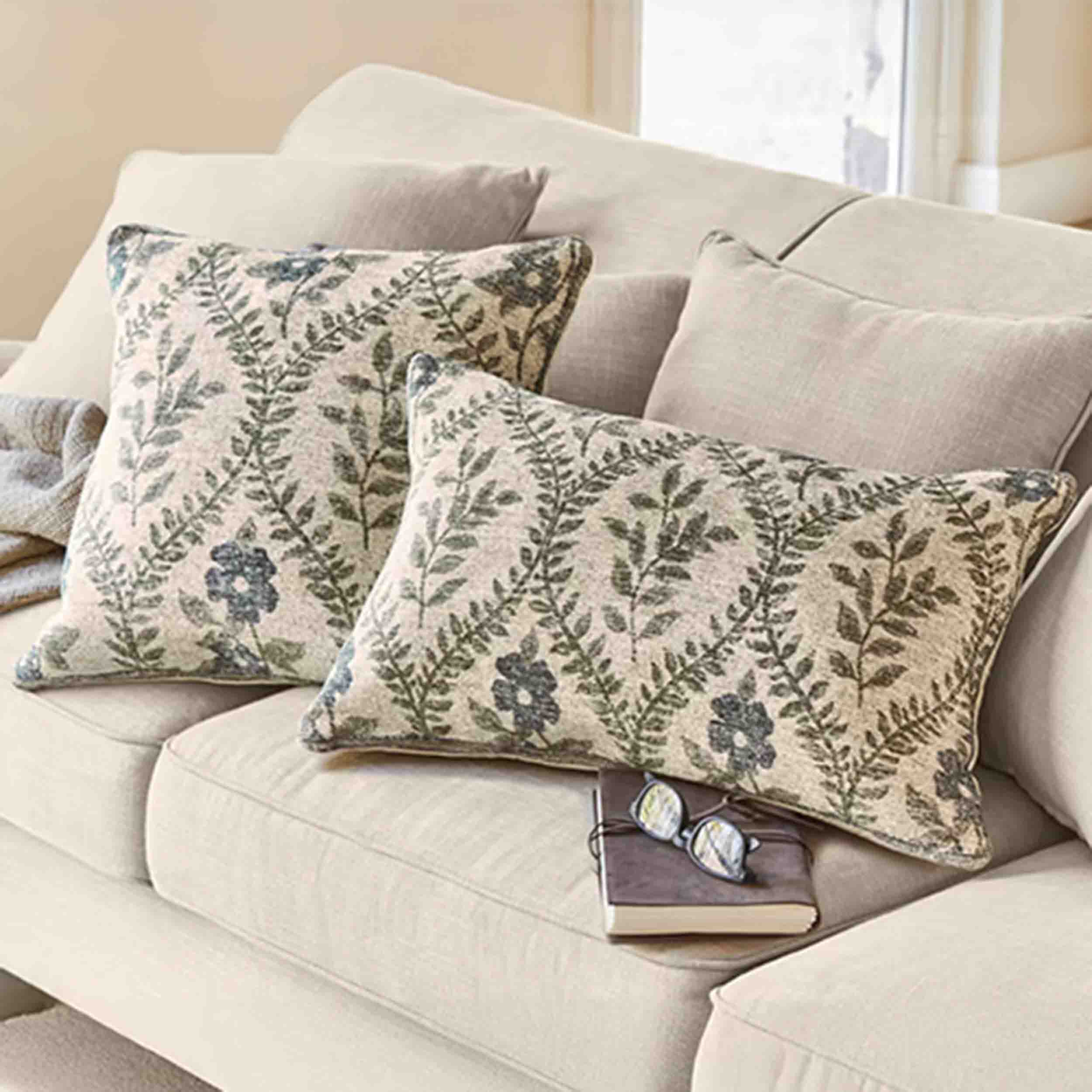 Beiges Sofa mit dekorativen Kissen in Blatt- und Blumenmuster, gemütliches Wohnzimmer mit Textilien