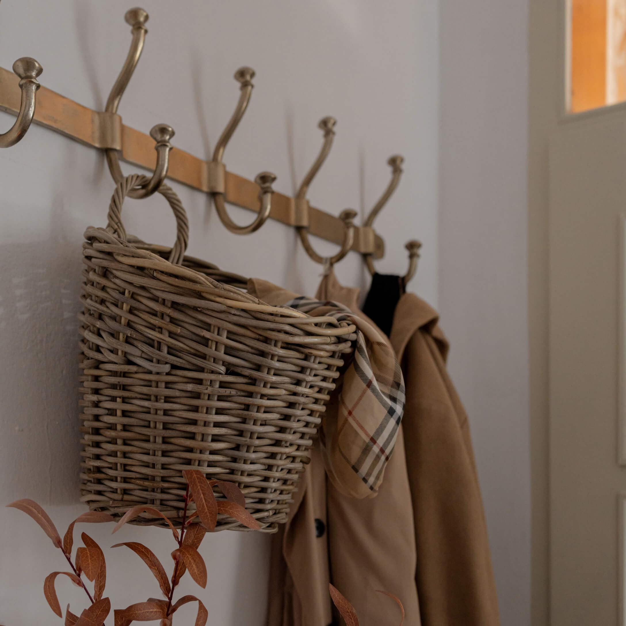 Weidenkorb an Messinggarderobe mit beigem Mantel und kariertem Schal