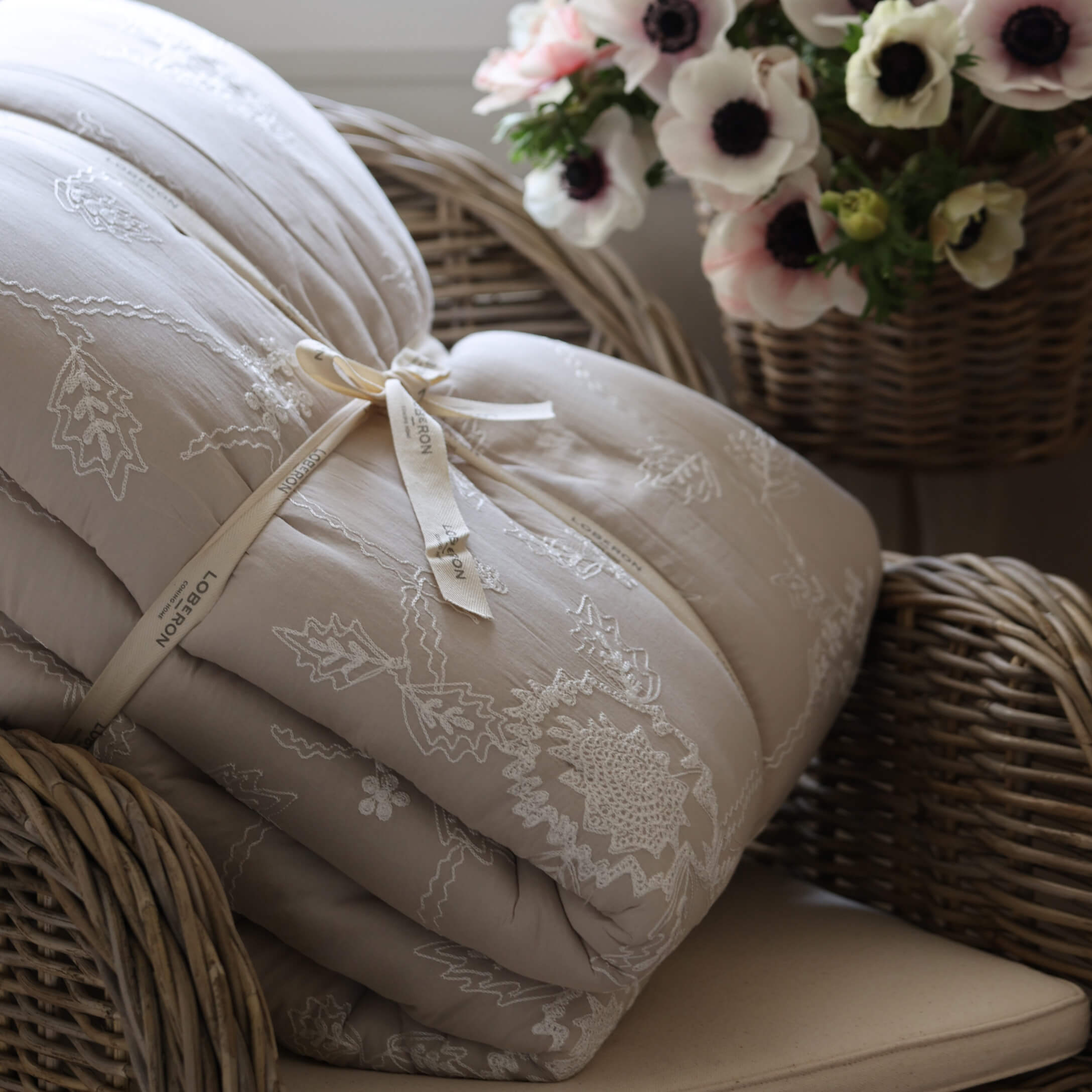 Beige gesteppte Tagesdecke mit Stickerei auf Korbsessel neben Blumenkorb, gemütliche Wohnraumdeko