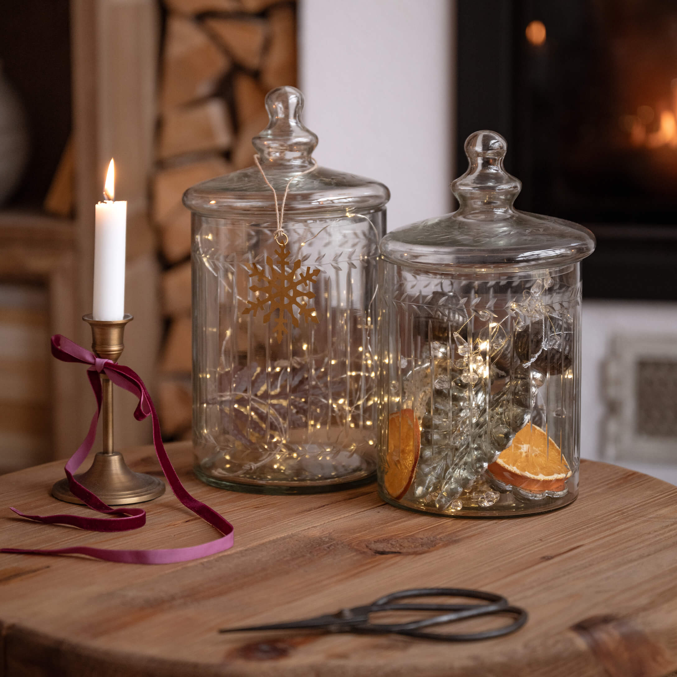 Transparente Glasbehälter mit Deckeln auf Holztisch, dekoriert mit Lichterketten und Kerze