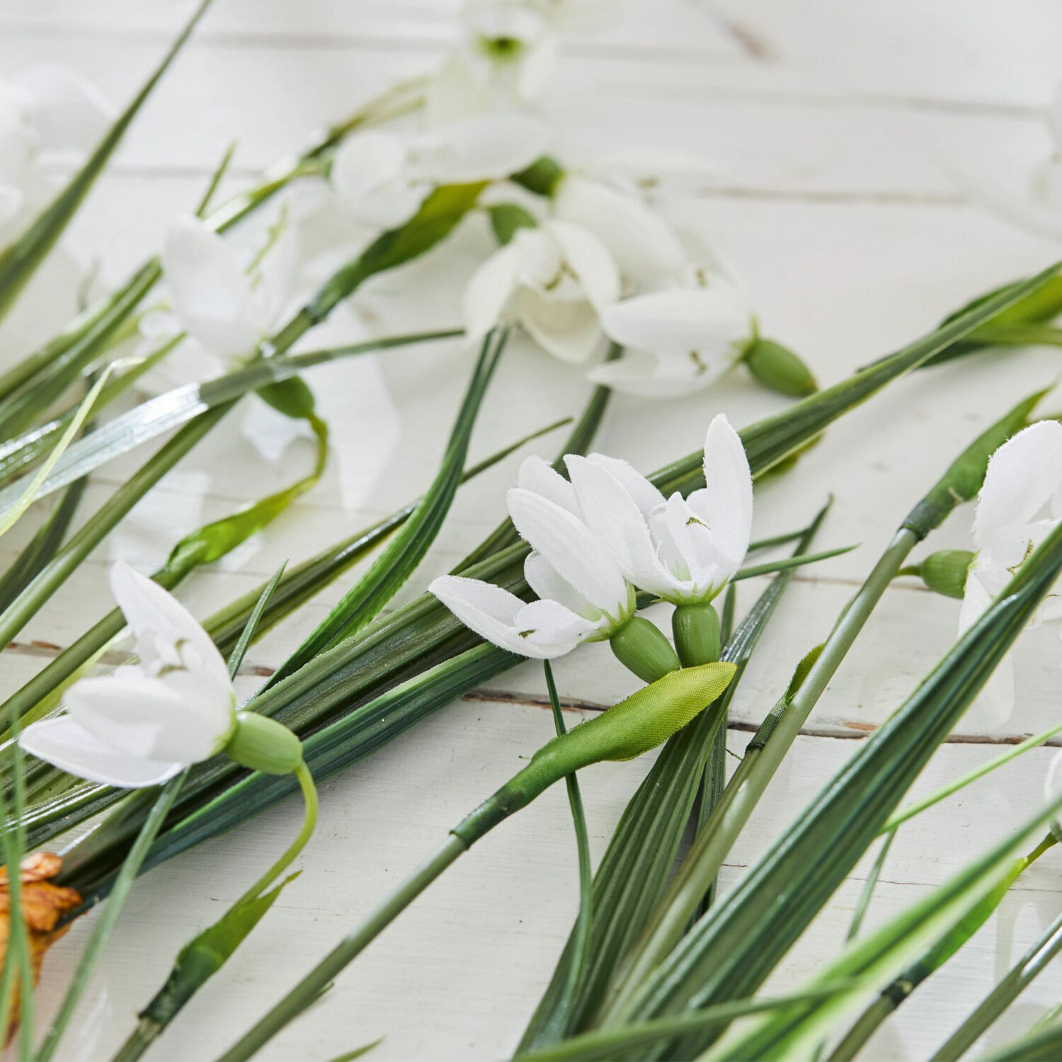 Weiße künstliche Blumen mit grünen Stielen auf hellem Hintergrund, Frühlingsdekoration für Zuhause