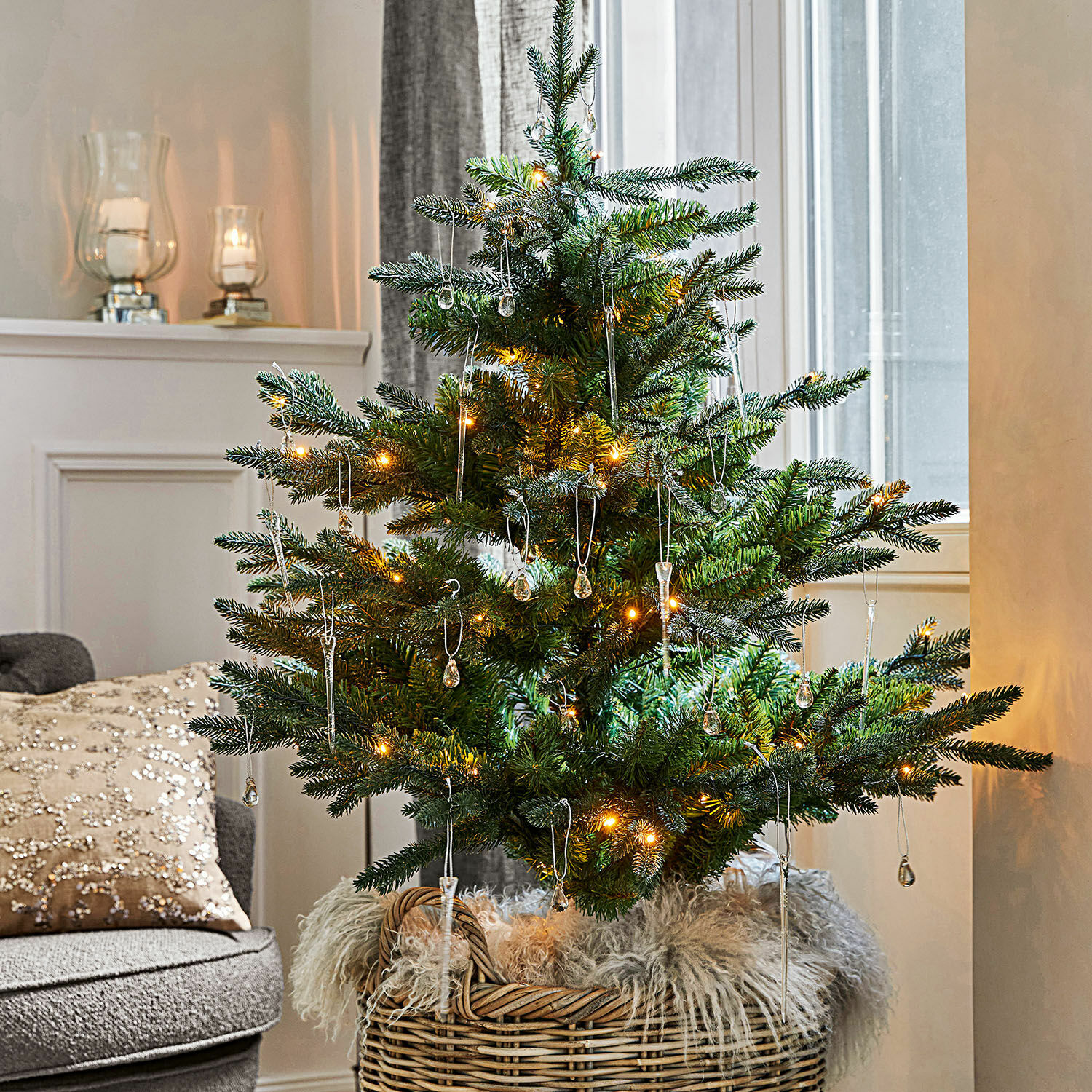 Kleiner grüner Weihnachtsbaum im Korb mit warmen Lichtern und gläsernen Christbaumschmuck