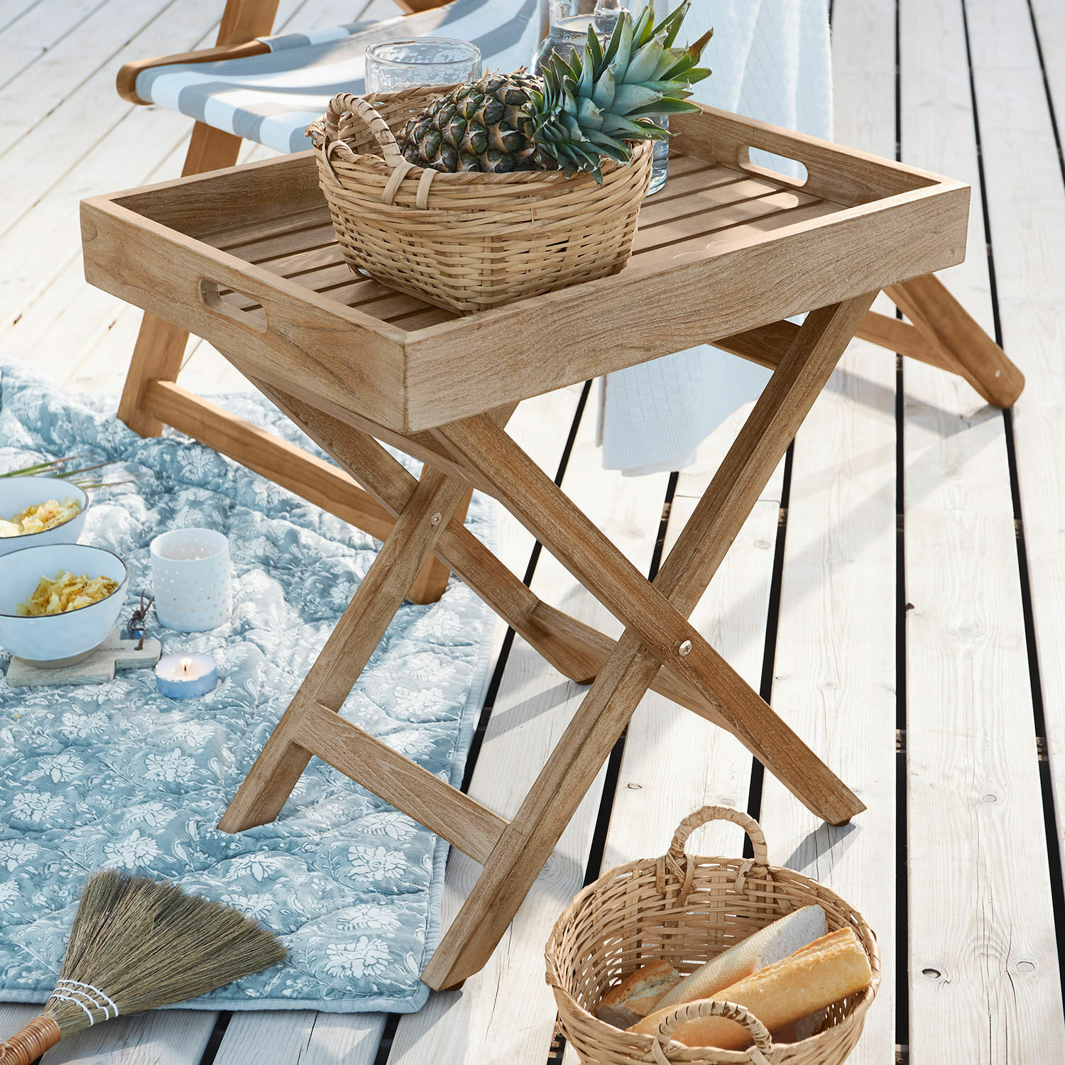 Klappbarer Teakholz-Tisch in Naturfarbe mit Korb und Ananas auf hellem Holzdeck im Freien