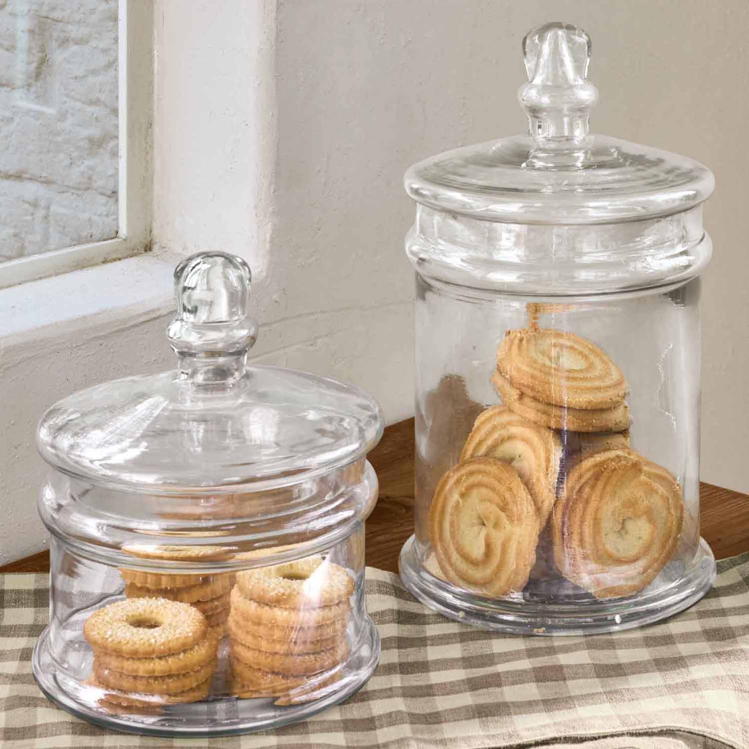 Zwei transparente Glasbehälter mit Deckeln gefüllt mit Keksen auf kariertem Tuch auf Holztisch