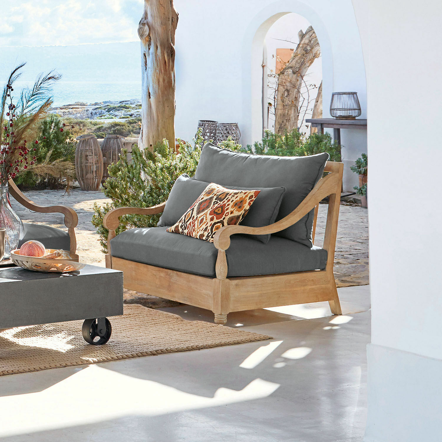 Sessel Montcassin Gartensofa aus Holz mit grauen Polstern und dekorativem Kissen in warmen Farben