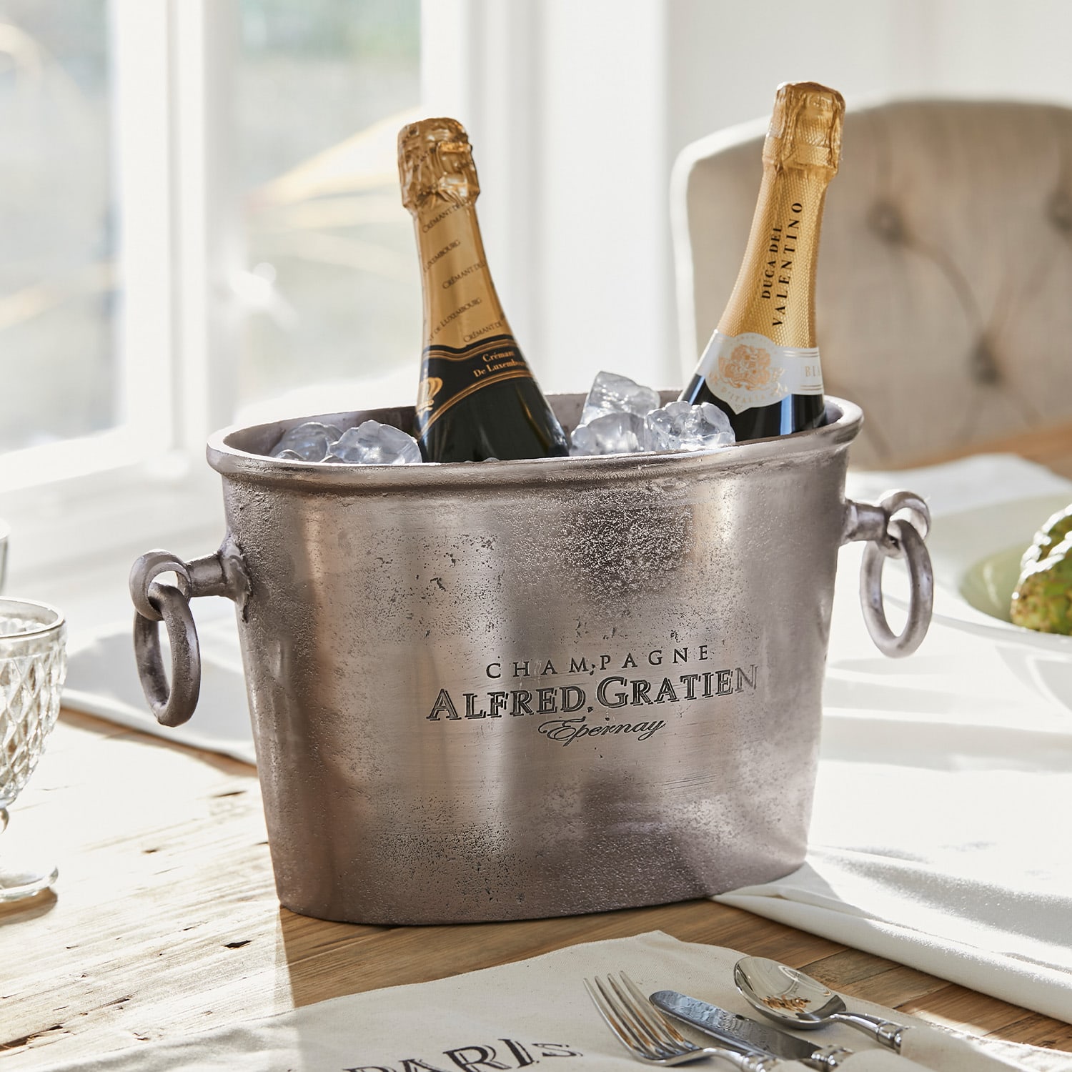 Metall Champagnerkühler mit zwei Flaschen und Eis auf Holztisch in hellem Raum