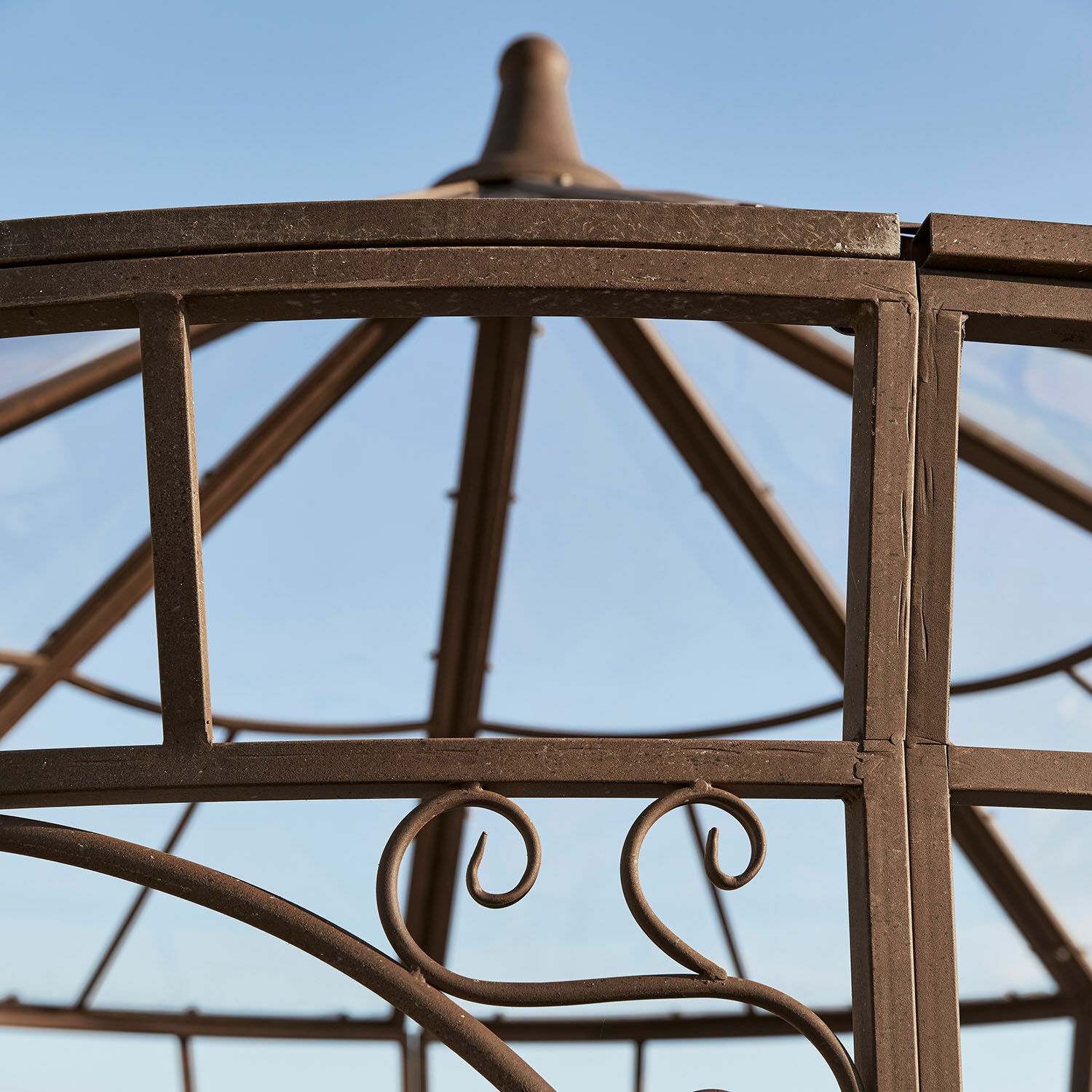 Braune Metallkonstruktion eines Pavillons mit dekorativen Schnörkeln vor blauem Himmel