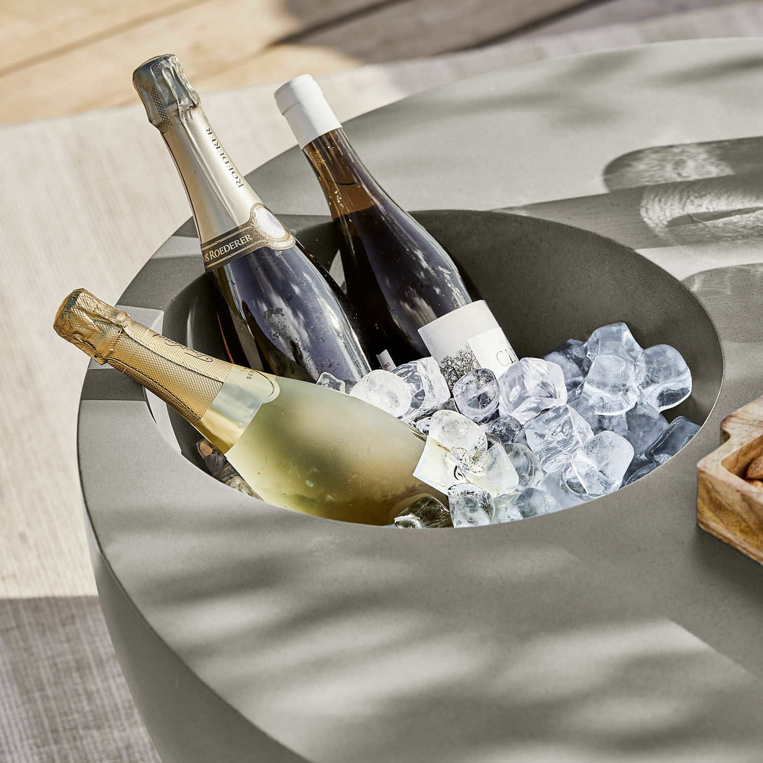 Grauer Betontisch mit integriertem Flaschenkühler, gefüllt mit Wein- und Champagnerflaschen auf Eis
