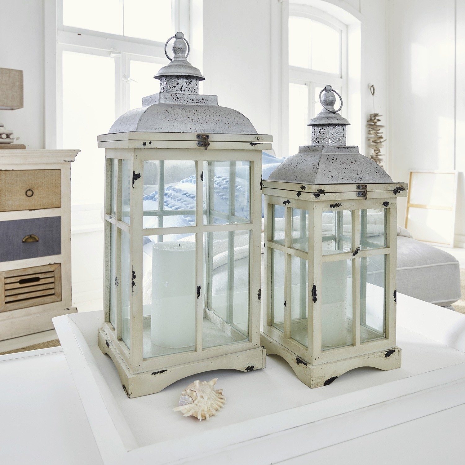 Zwei cremefarbene Vintage-Metalllaternen mit weißen Kerzen auf Tisch in hellem Raum