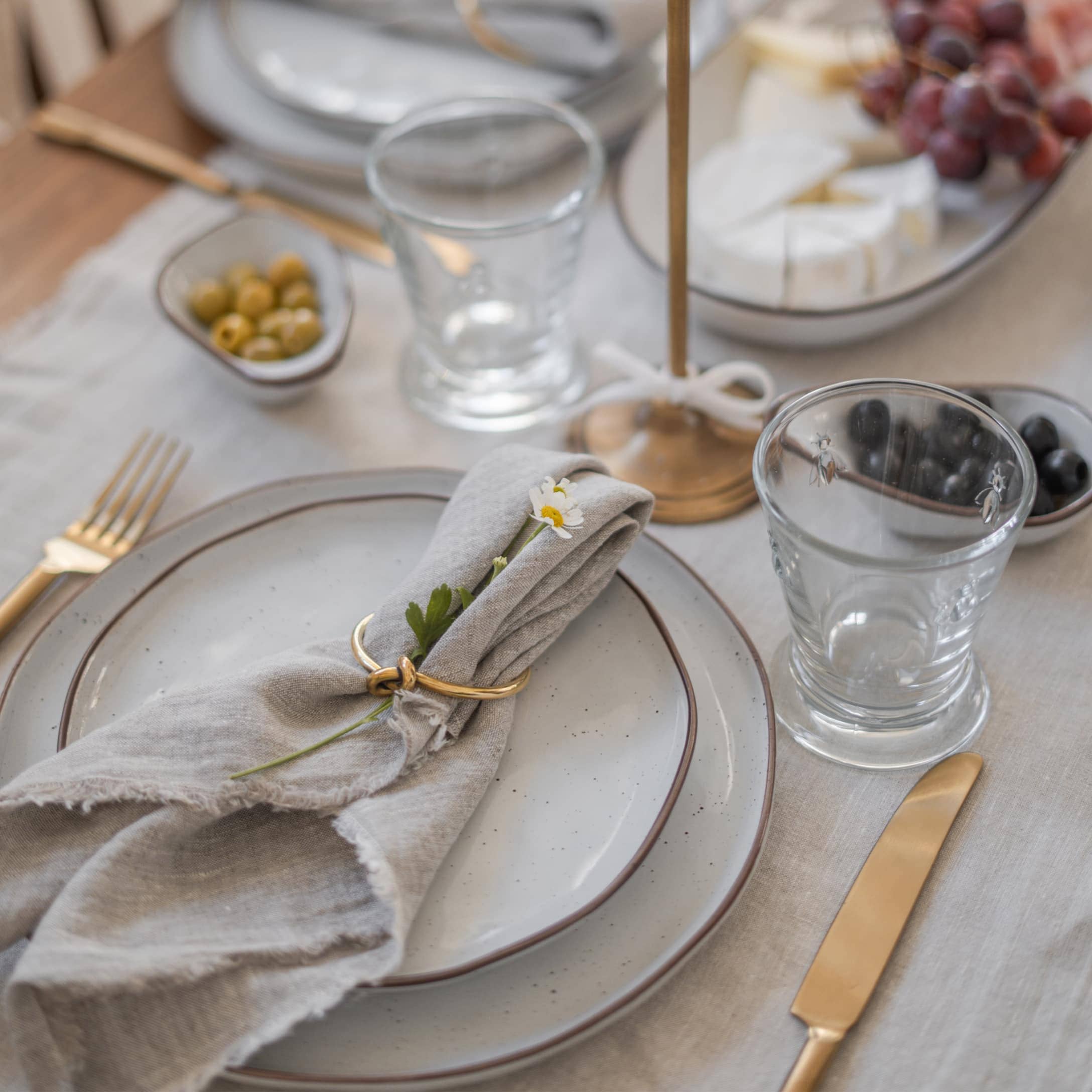 Elegantes Tischgedeck mit grauen Tellern, goldenen Bestecken und Leinenserviette mit Blume