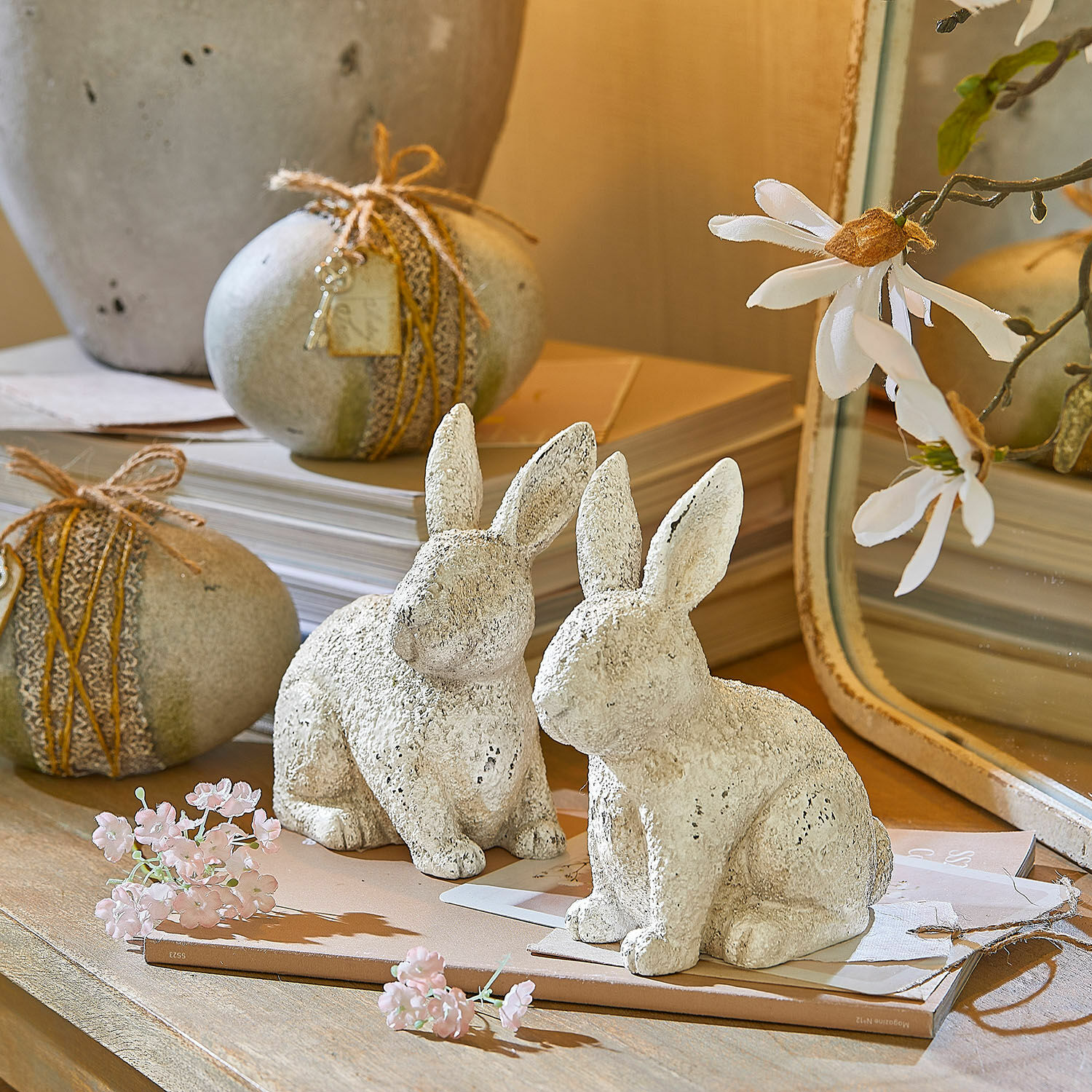 Weiße Deko-Kaninchen aus Stein auf Holztisch mit Blumen und Büchern als Frühlingsdeko