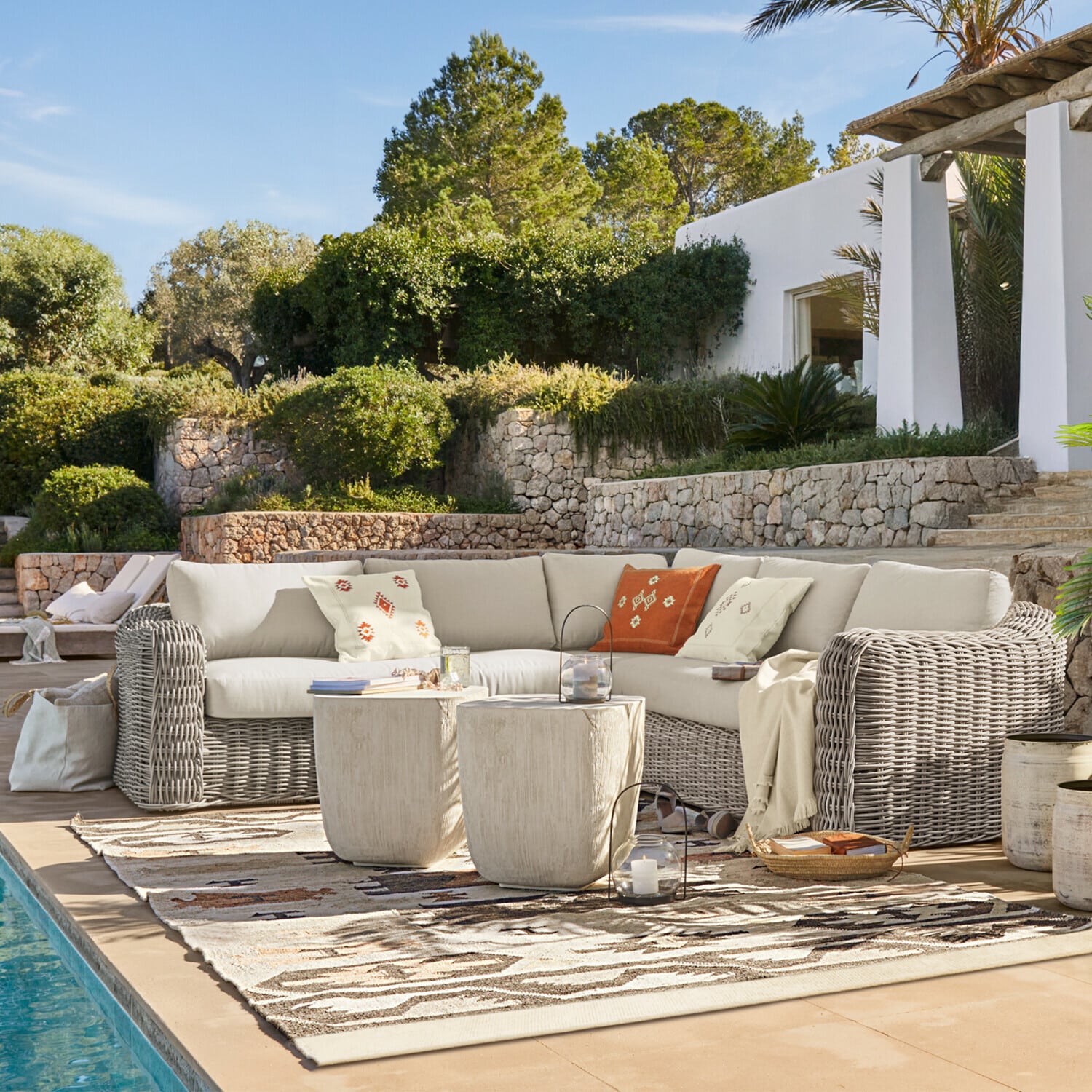 Gartenmöbel-Set aus grauem Rattan mit cremefarbenen Polstern und warmen Dekokissen am Pool