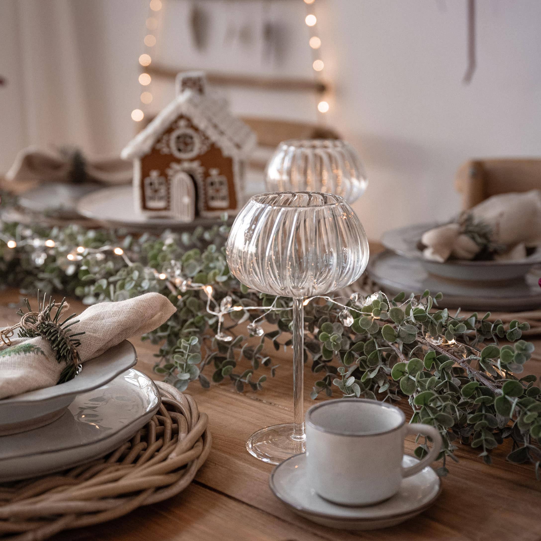 Weihnachtstisch mit dekorativen Glaswindlichtern und natürlichen grünen Zweigen für festliche Stimmung
