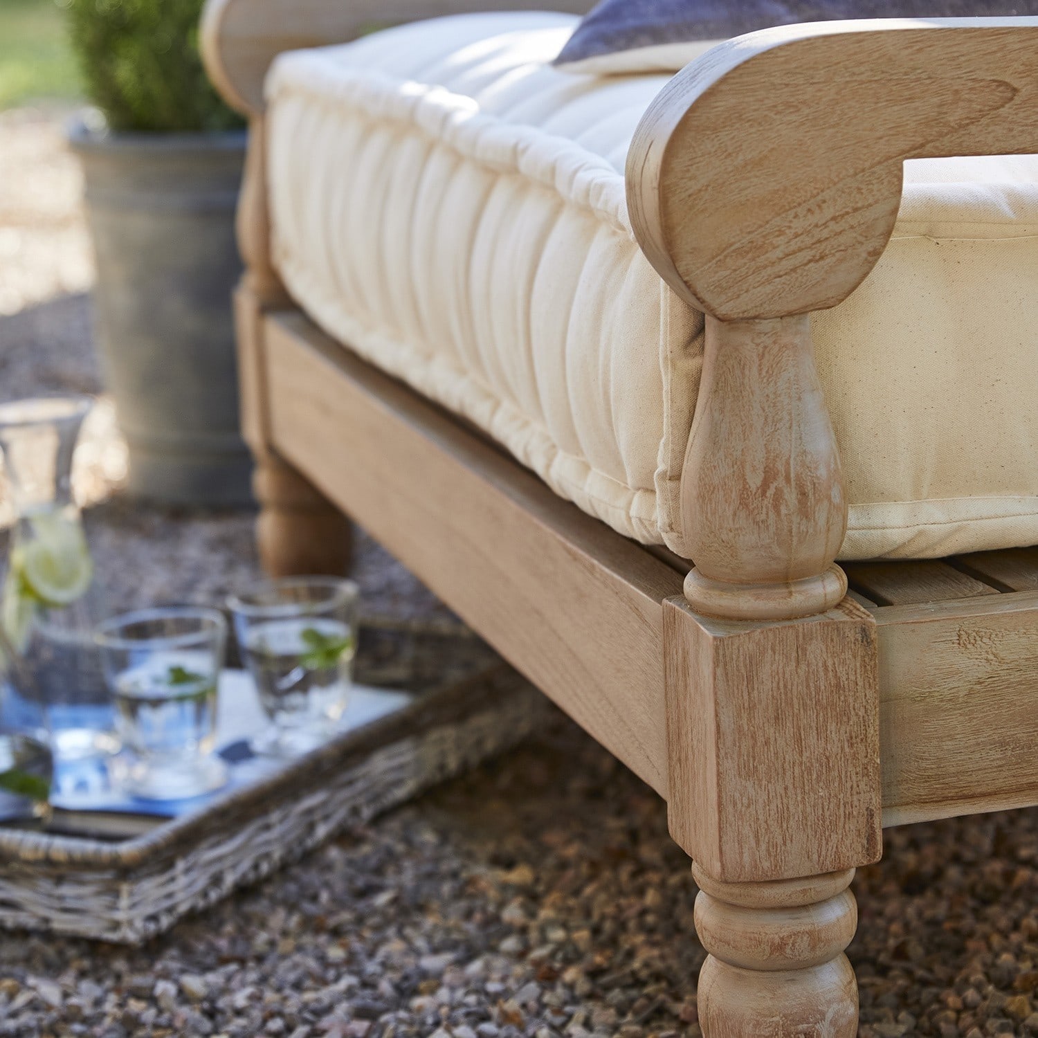 Outdoor-Sofa mit cremefarbenem Polster und hellem Holzrahmen auf Kiesboden