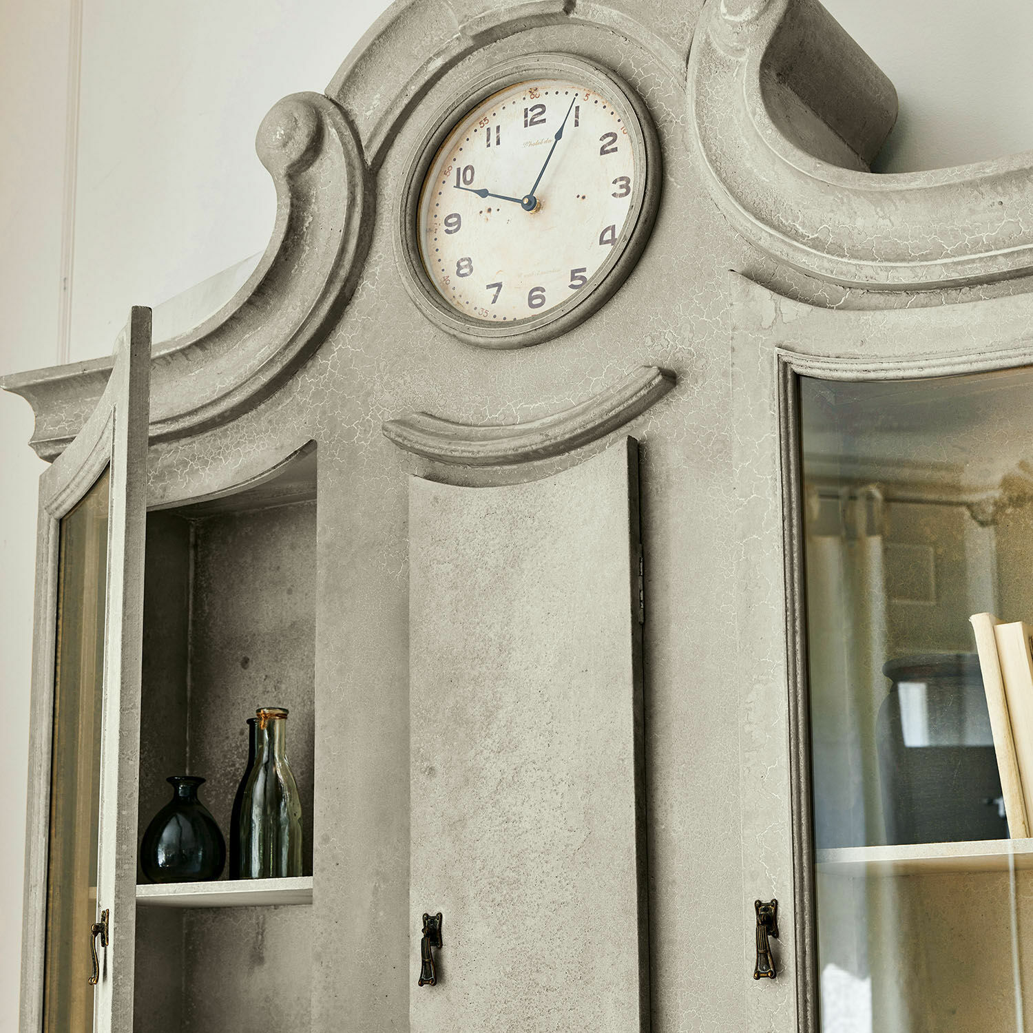 Grauer Schrank mit integrierter Uhr und Glastüren im Vintage-Stil, dekorative Flaschen innen