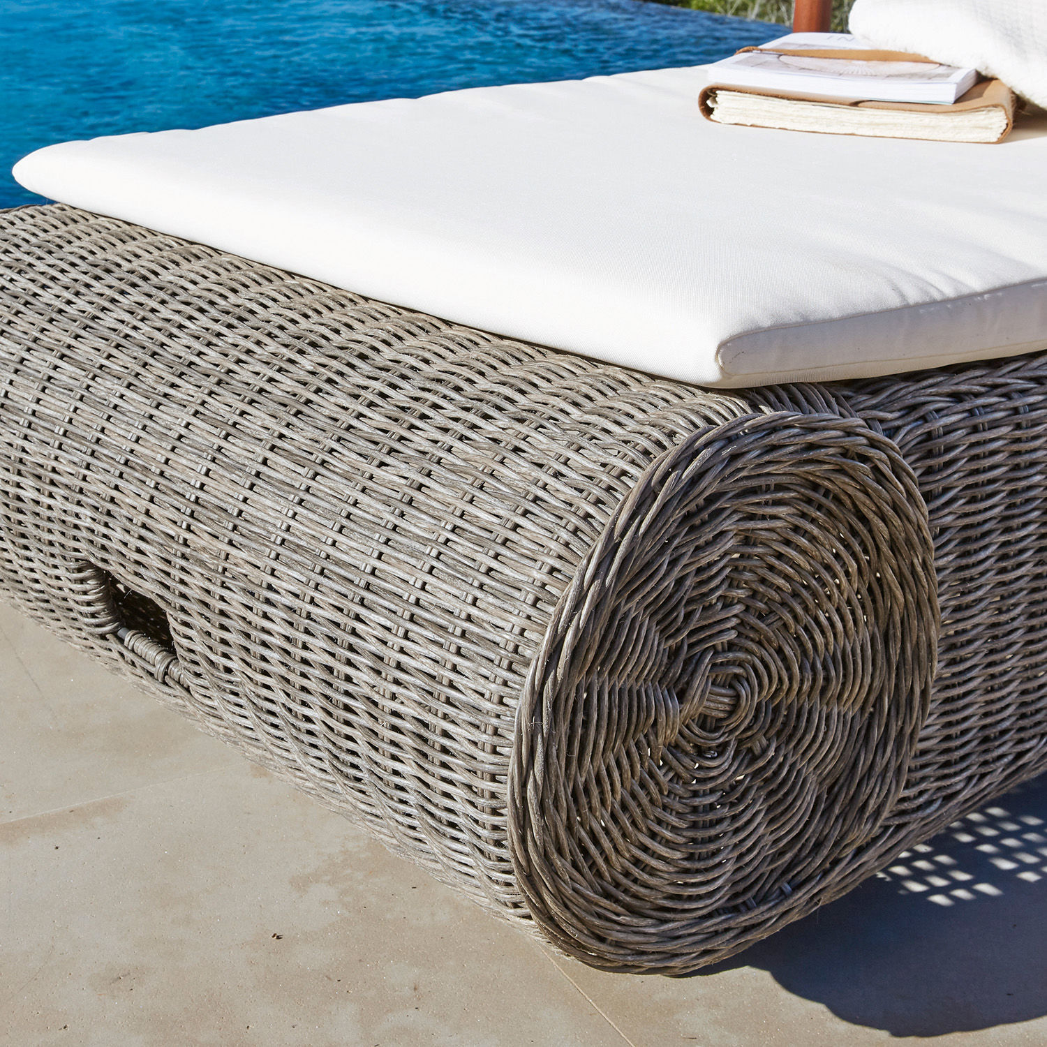Graues Rattan-Liege mit weißer Polsterung, ideal zum Entspannen im Außenbereich am Pool
