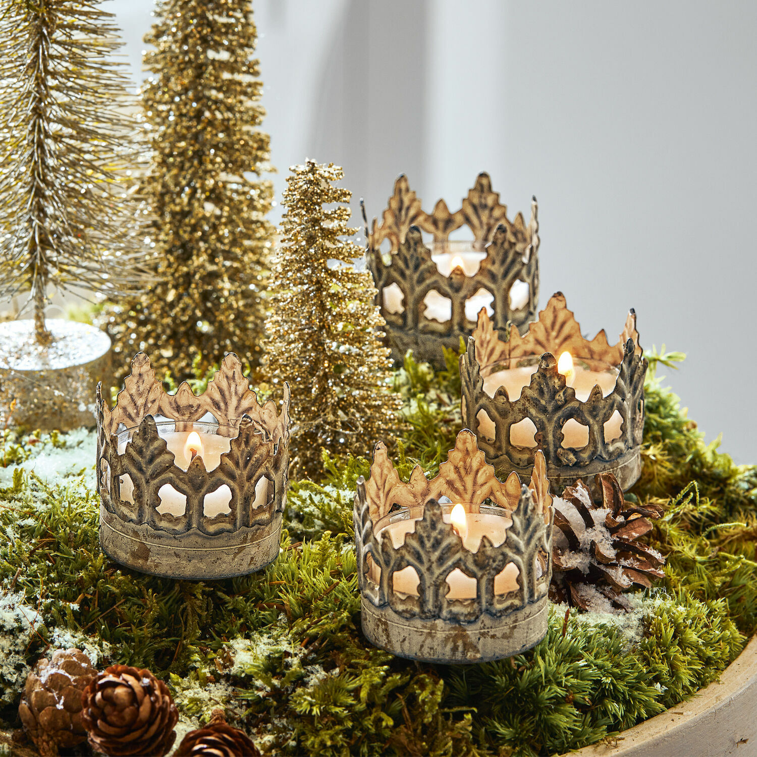 Steckwindlicht 4er Set Groisy Metall-Kerzenhalter in Kronenform auf grünem Moos mit Weihnachtsdeko und brennenden Kerzen