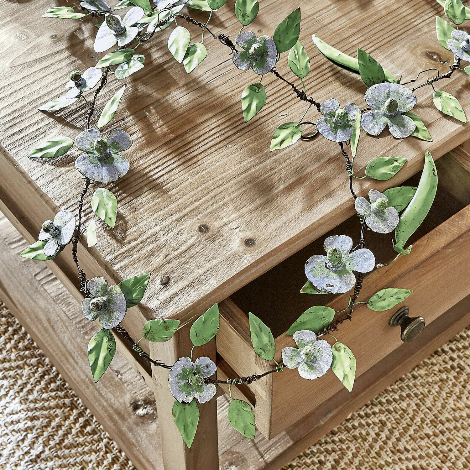 Dekorative Metallgirlande mit weißen Blumen und grünen Blättern auf Holztisch