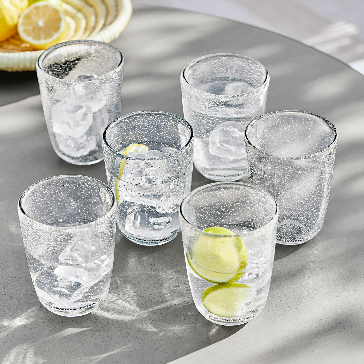 Glas 6er Set Parilly Sechsteiliges Set Gläser aus klarem Glas mit Luftblasen, Eiswürfeln und Zitronenscheiben auf grauem Tisch