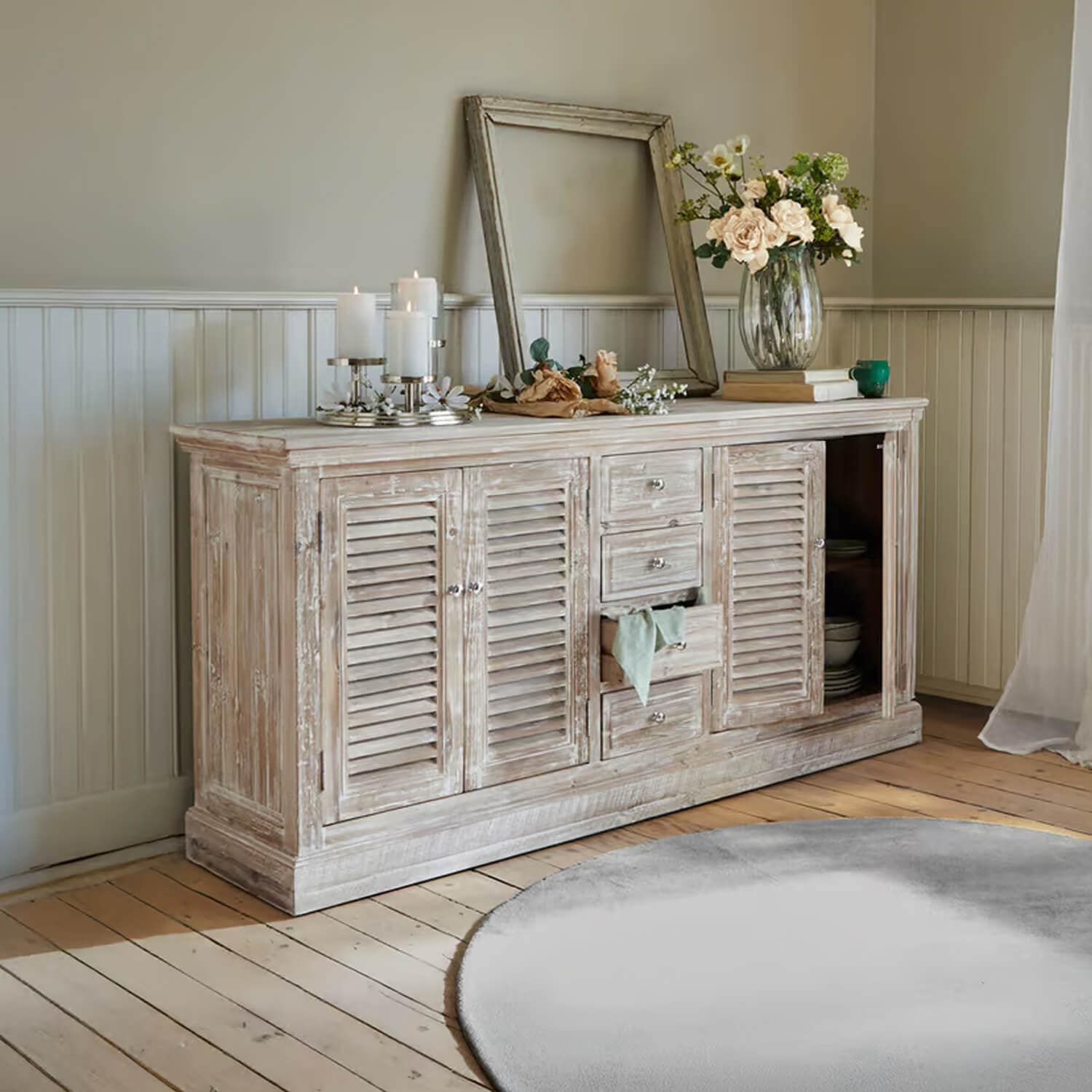 Rustikales Sideboard aus Holz mit weißem Used-Look, dekoriert mit Kerzen und Blumen im Wohnzimmer