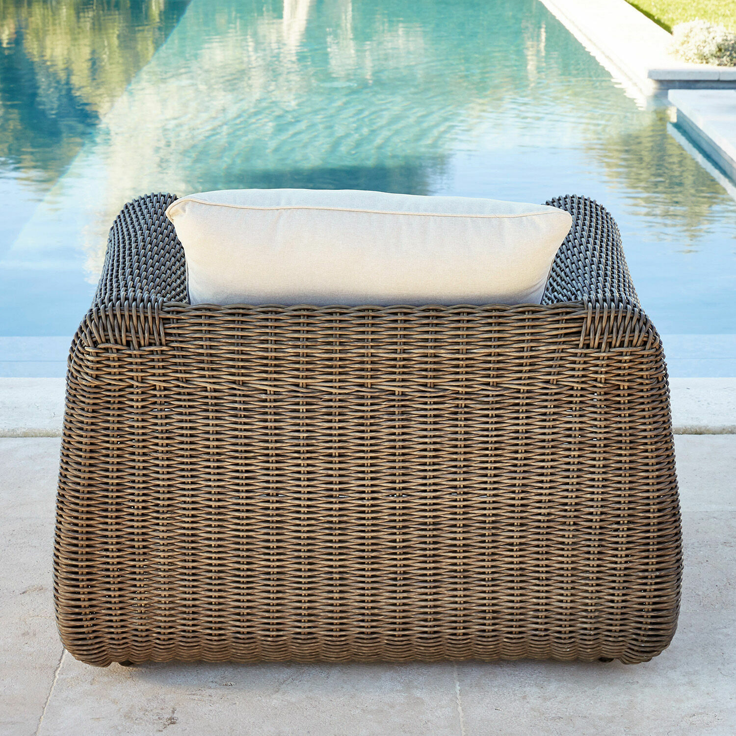 Gartenfauteuil aus braunem Rattan mit hellem Kissen am Pool, Outdoor-Möbel