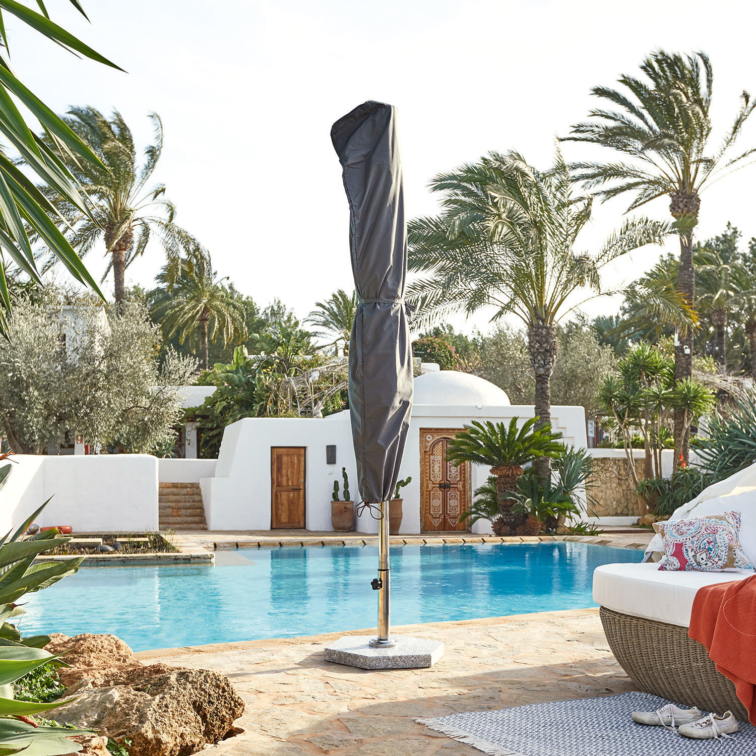 Graue Schutzhülle für Sonnenschirm am Pool mit Steinboden und Rattanmöbeln im Außenbereich