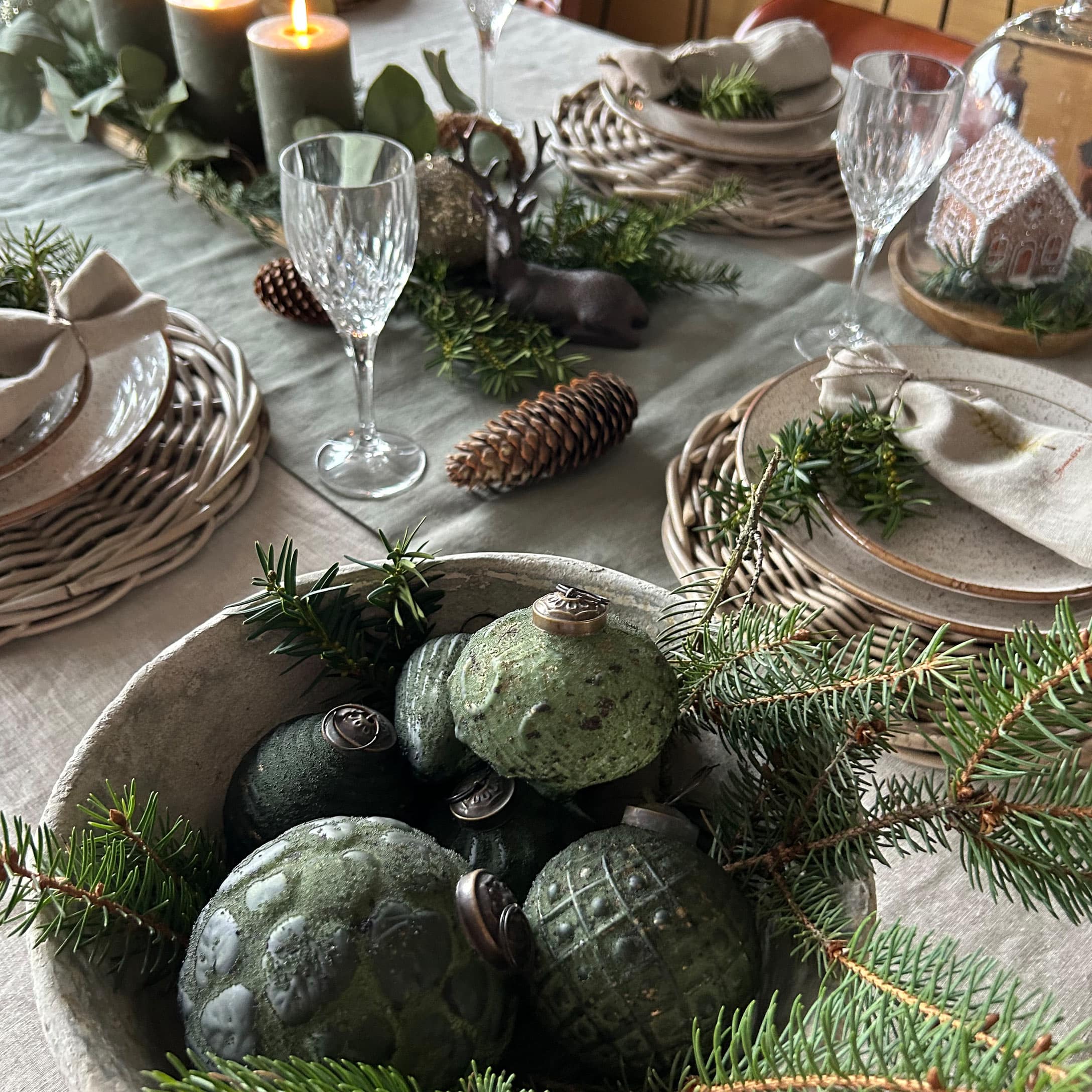 Grüne Keramik-Weihnachtskugeln in Schale mit Tannenzweigen auf festlich gedecktem Tisch