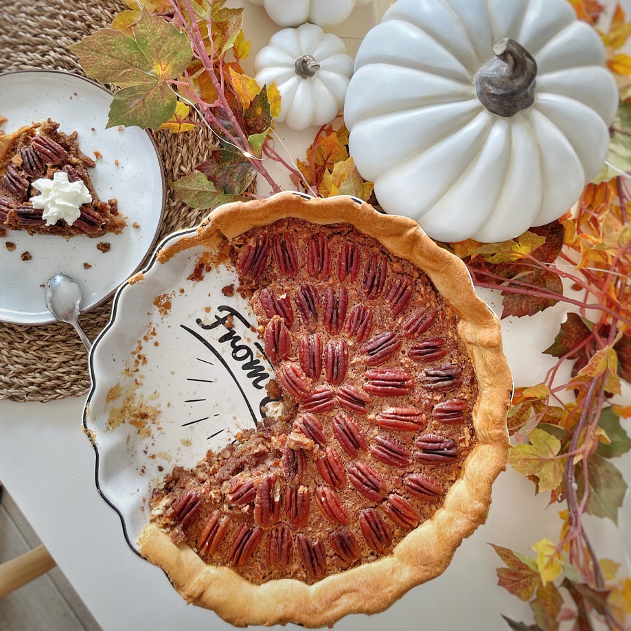 Pekannusskuchen auf Teller mit herbstlicher Dekoration und weißen Kürbissen