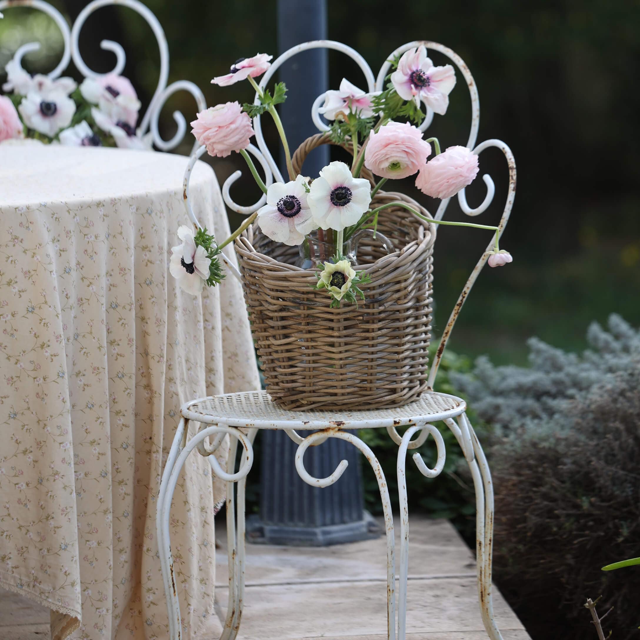 Weidenkorb mit rosa und weißen Blumen auf weißem Metallstuhl im Garten