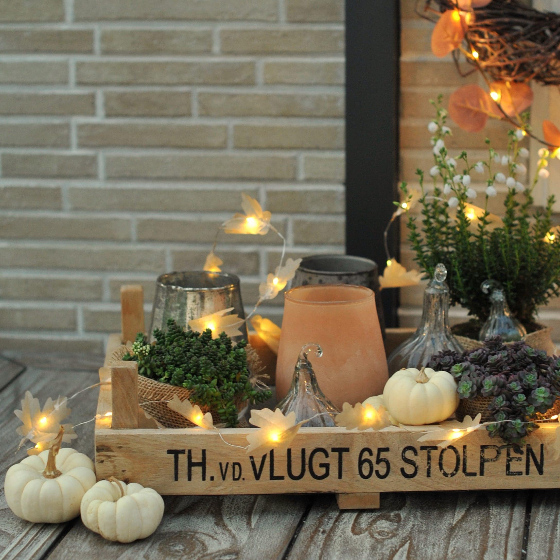 Holztablett mit herbstlicher Dekoration, weißen Kürbissen, Pflanzen und LED-Lichterkette auf Holztisch