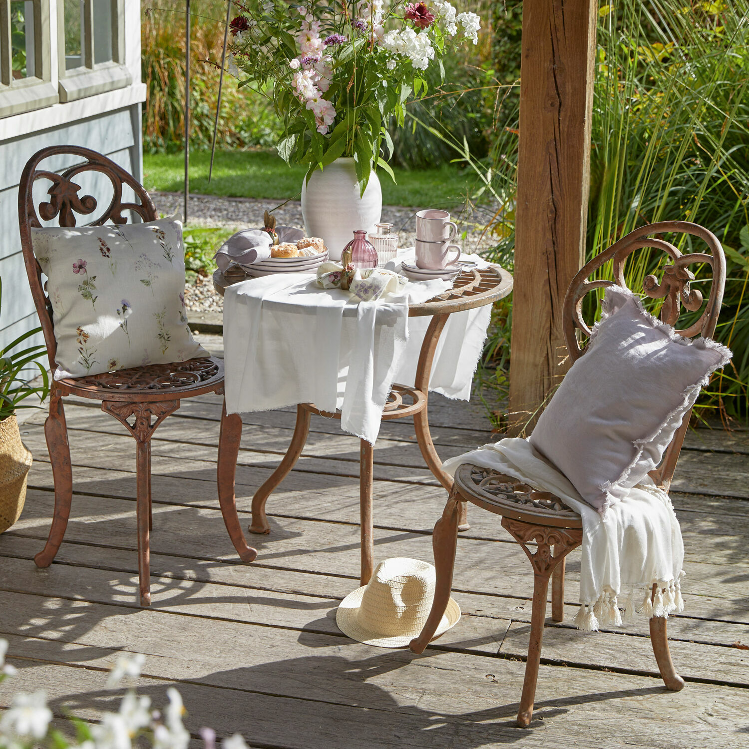 Gusseisernes Gartenmöbel-Set in Rostfarbe mit Kissen und weißem Tischläufer auf Holzterrasse