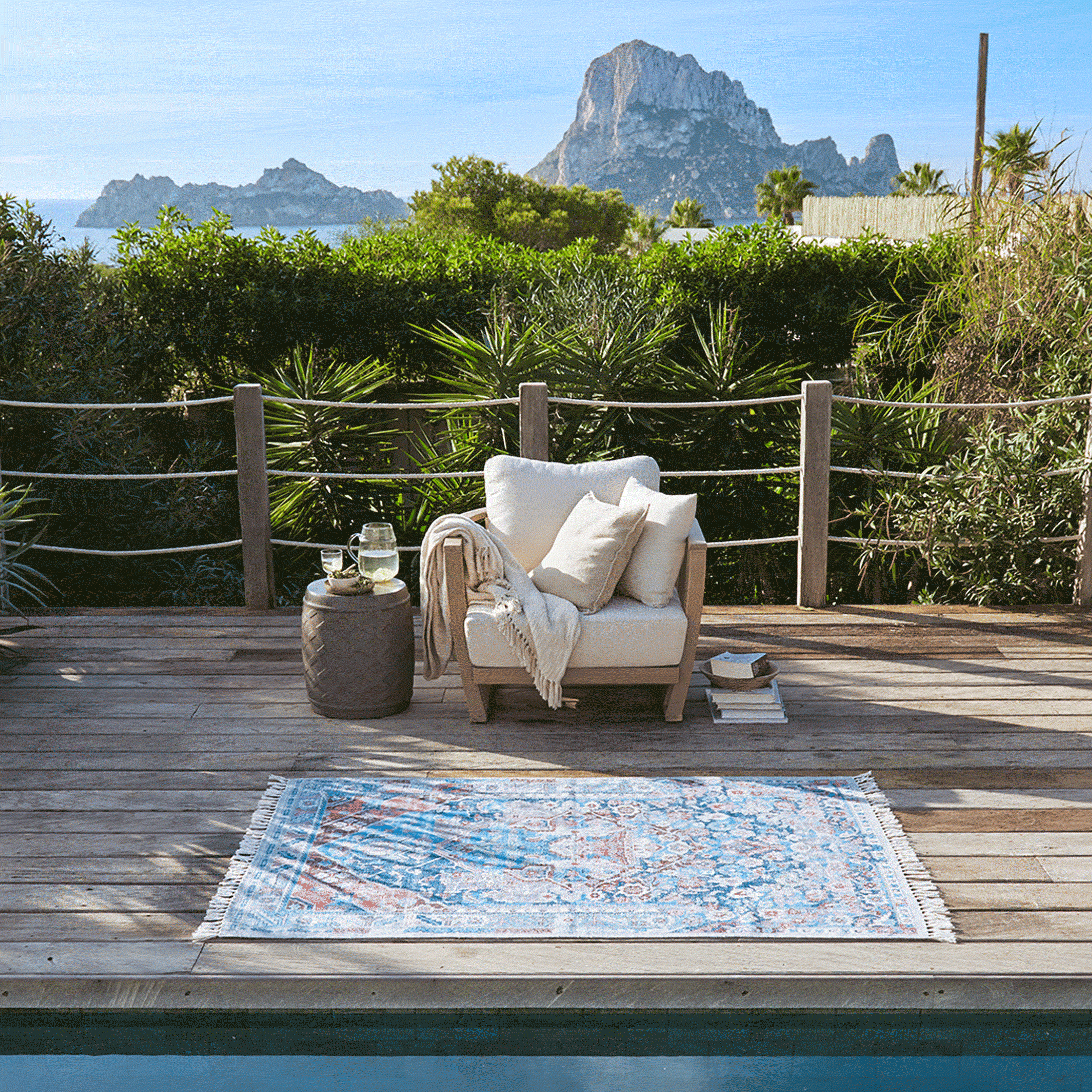 Holzterrasse mit weißem Sessel und buntem Teppich am Pool mit Bergblick