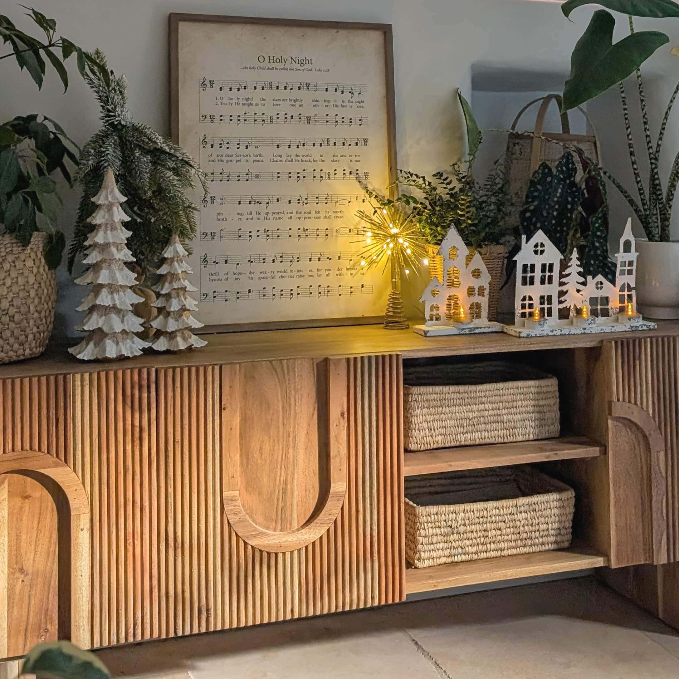 Holzkommode mit Weihnachtsdekoration, weißen Häusern und beleuchteten LED-Tannenbäumen