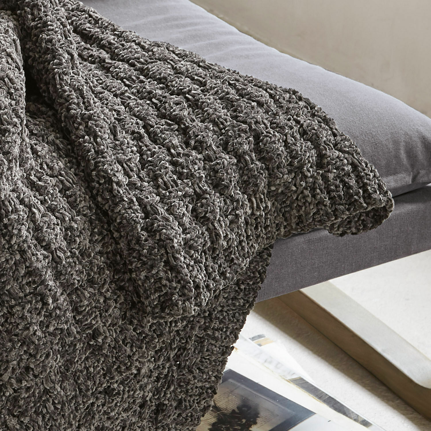 Grau gestrickte Kuscheldecke mit grobem Muster auf grauem Sofa für gemütliche Einrichtung