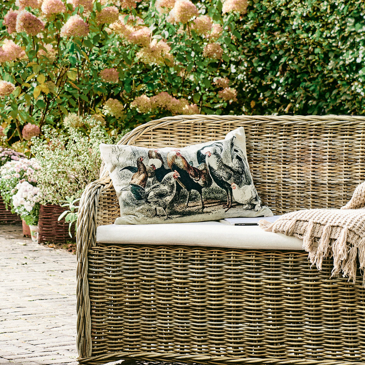 Garten mit Korbsofa und Kissen mit Hühnermotiv, natürliche Farben und Dekoration