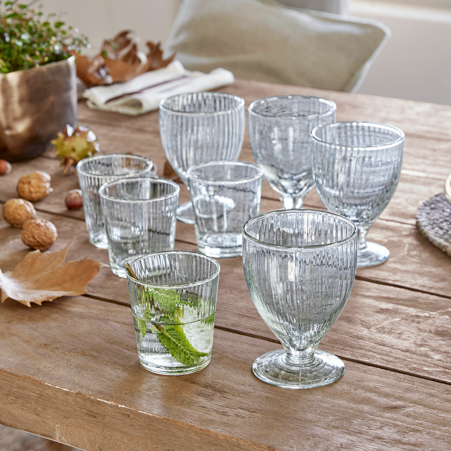 Set aus transparenten, gerillten Gläsern auf Holztisch mit herbstlicher Dekoration