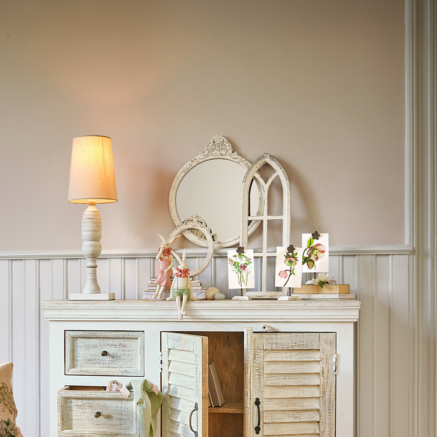 Weiße Holzkommode mit Lampe, Spiegeln und Vintage-Dekorationen für gemütliches Wohnzimmer