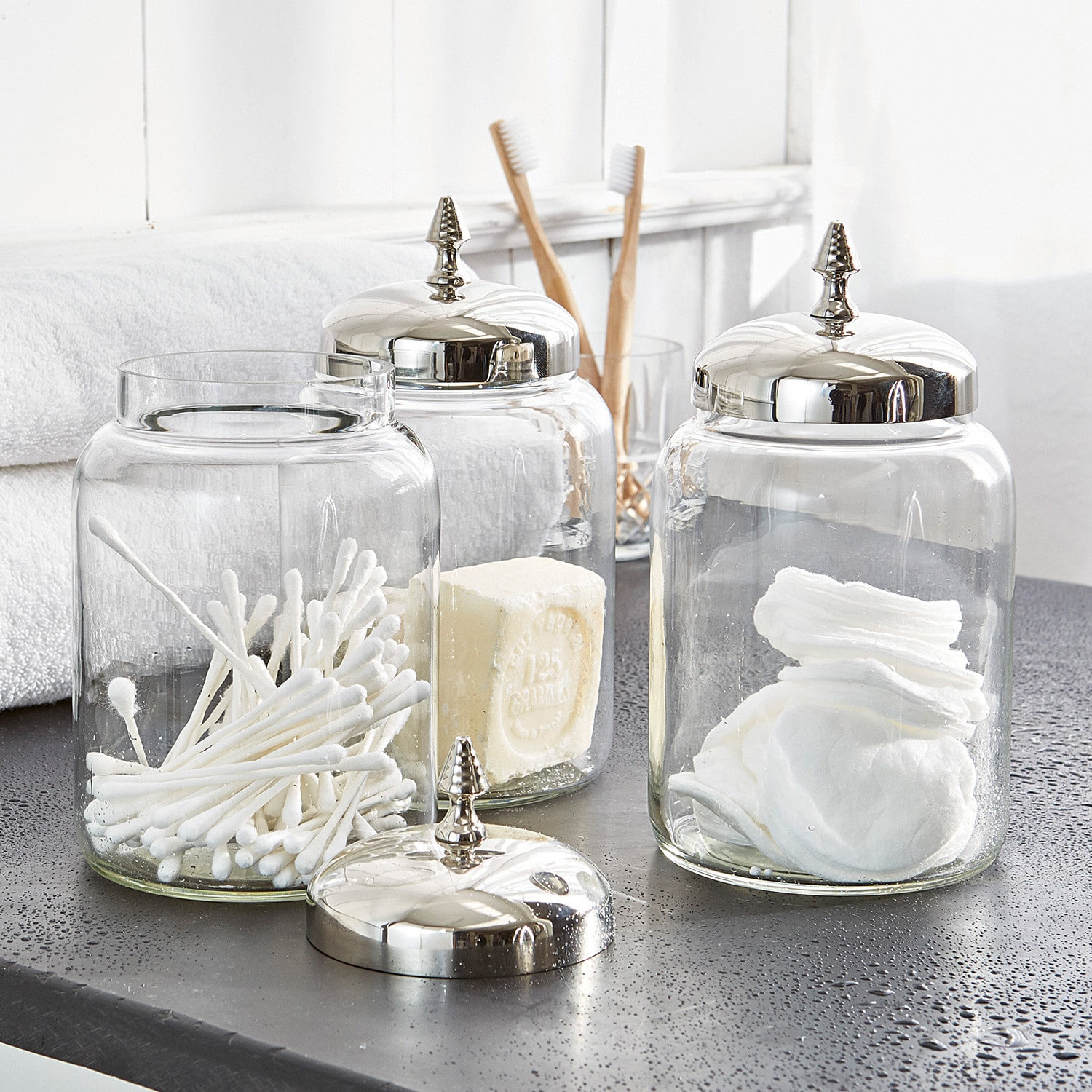 Glasbehälter mit silbernen Metalldeckeln für Wattepads und Wattestäbchen im Badezimmer