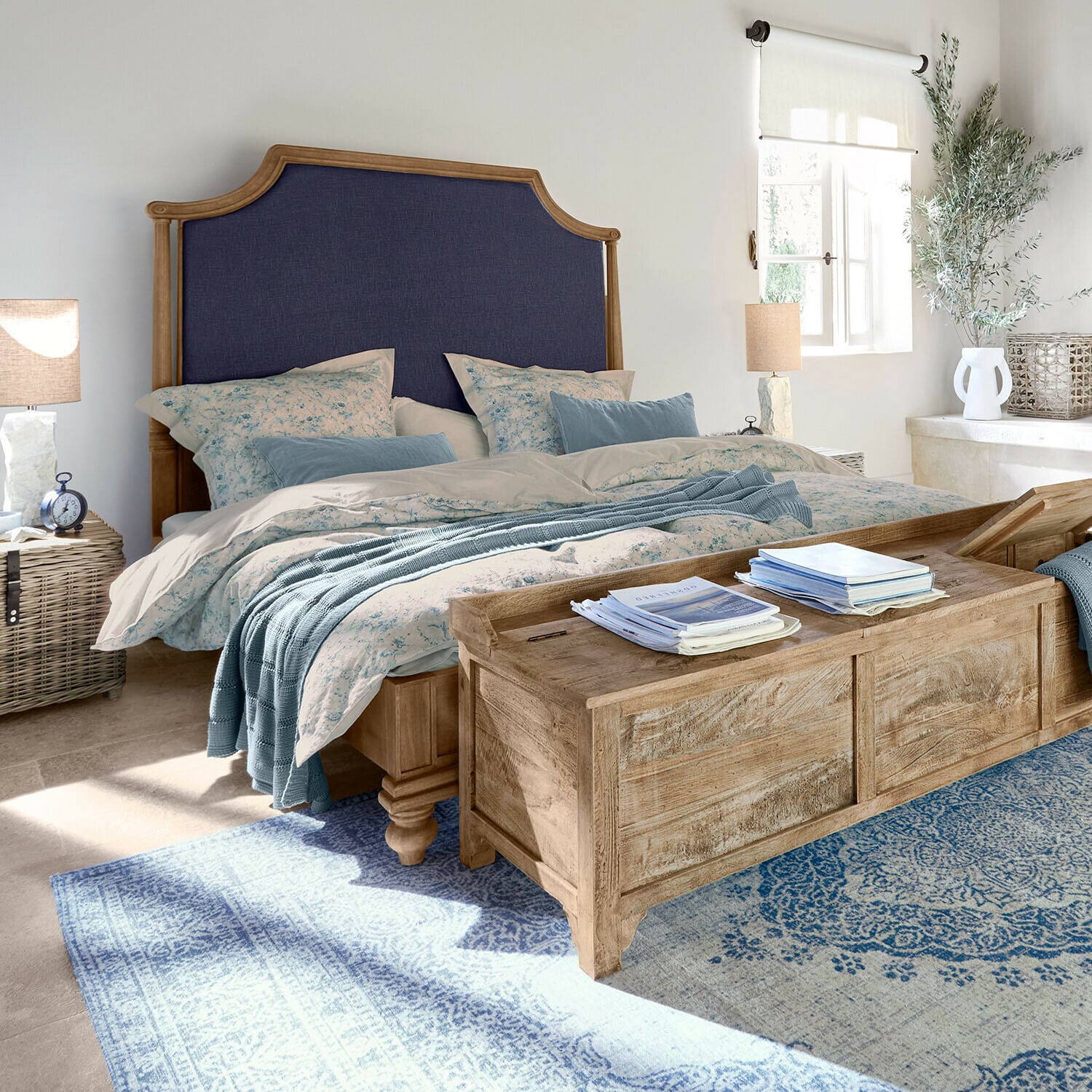 Schlafzimmer mit Holzbett, dunkelblau gepolstertem Kopfteil und blauem Teppich im Landhausstil