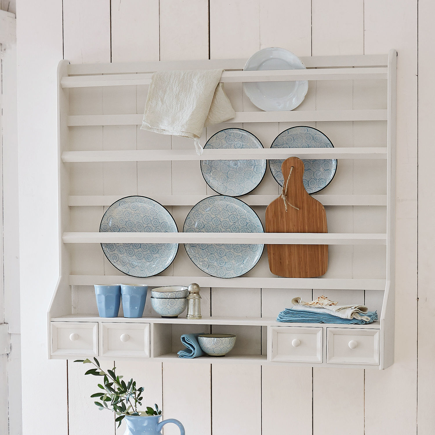 Weißes Holzregal mit blauen Keramiktellern, Schneidebrett und Küchenutensilien an der Wand