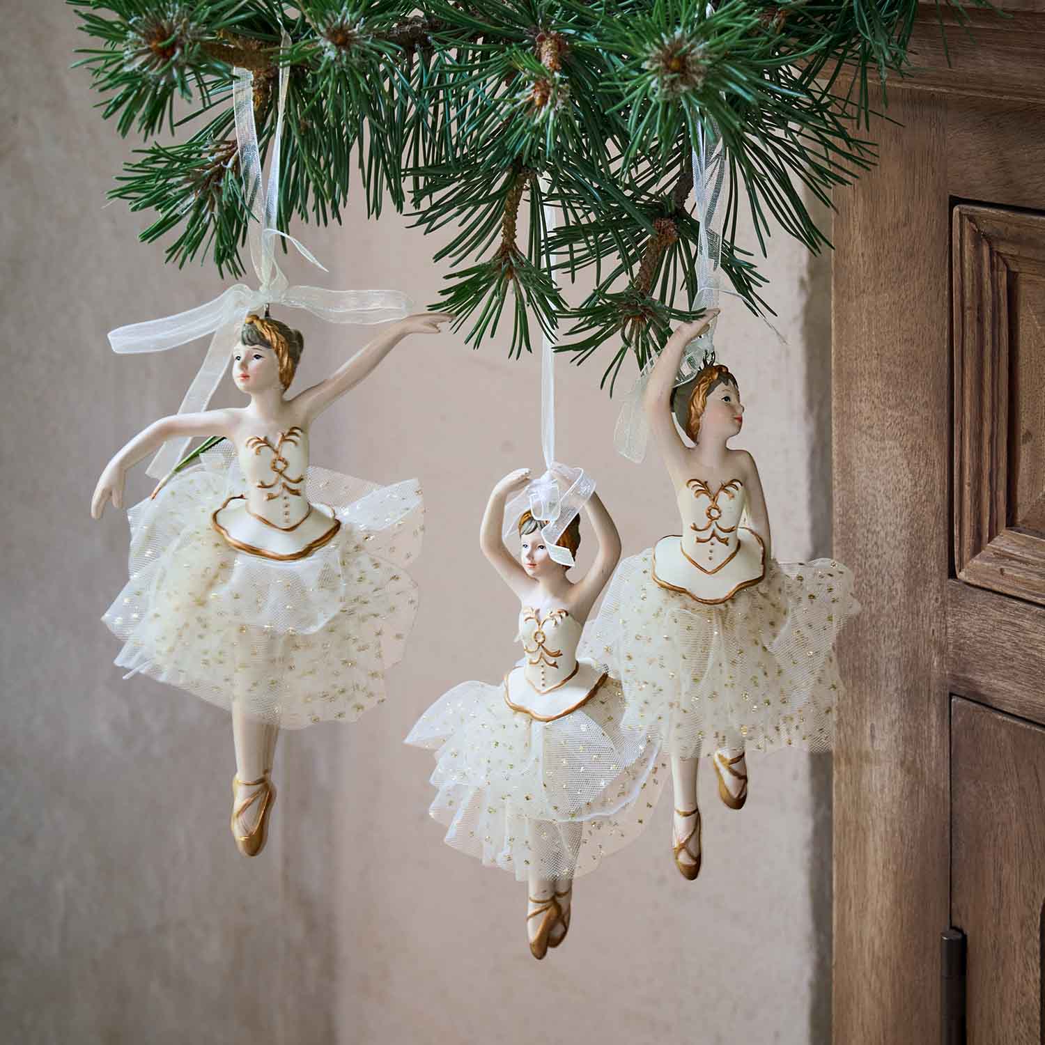 Drei weiße Ballerina-Figuren mit Tüllröcken und goldenen Details an einem Tannenzweig hängend