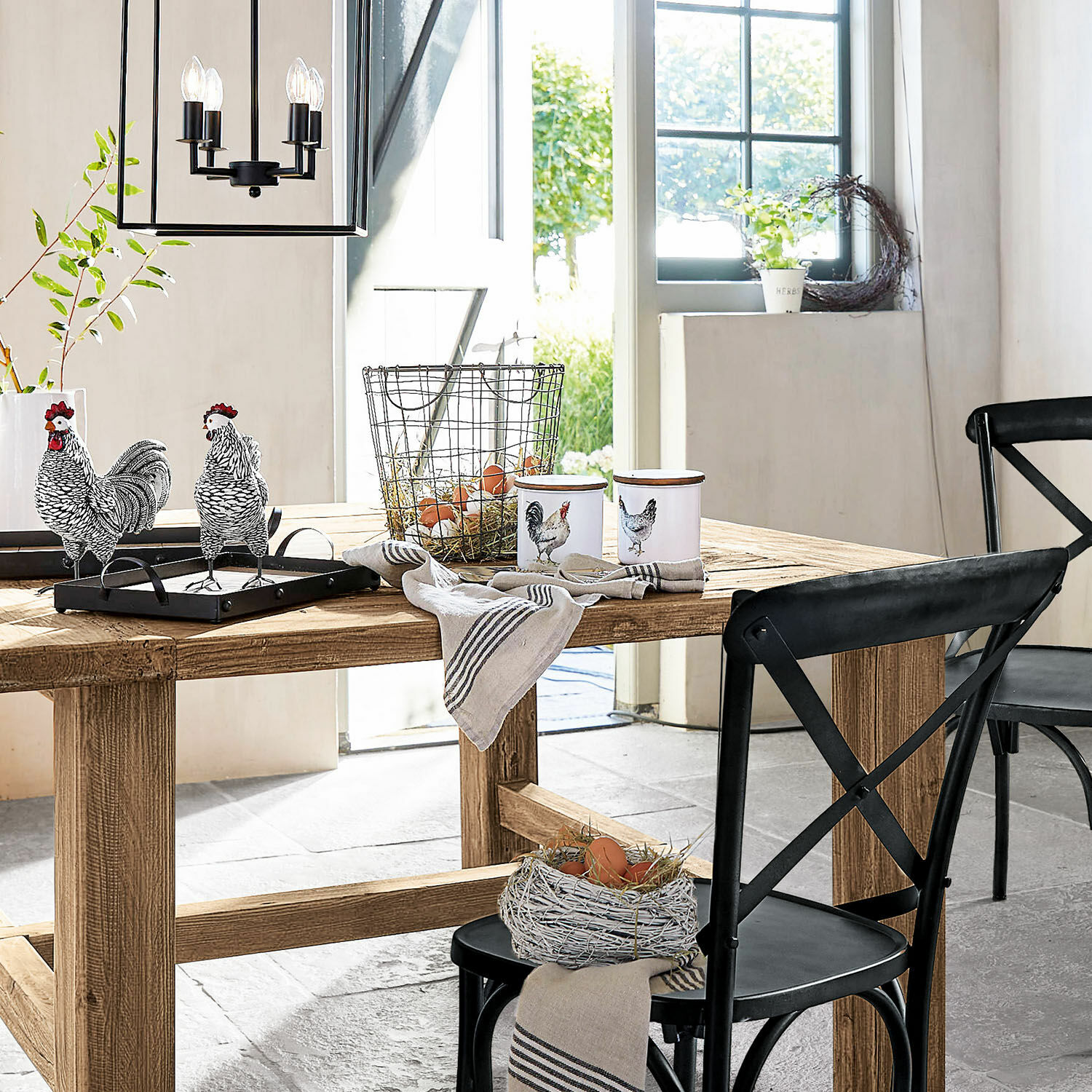 Rustikaler Holztisch mit schwarzen Metallstühlen und Hühner-Dekorationen in hellem Raum