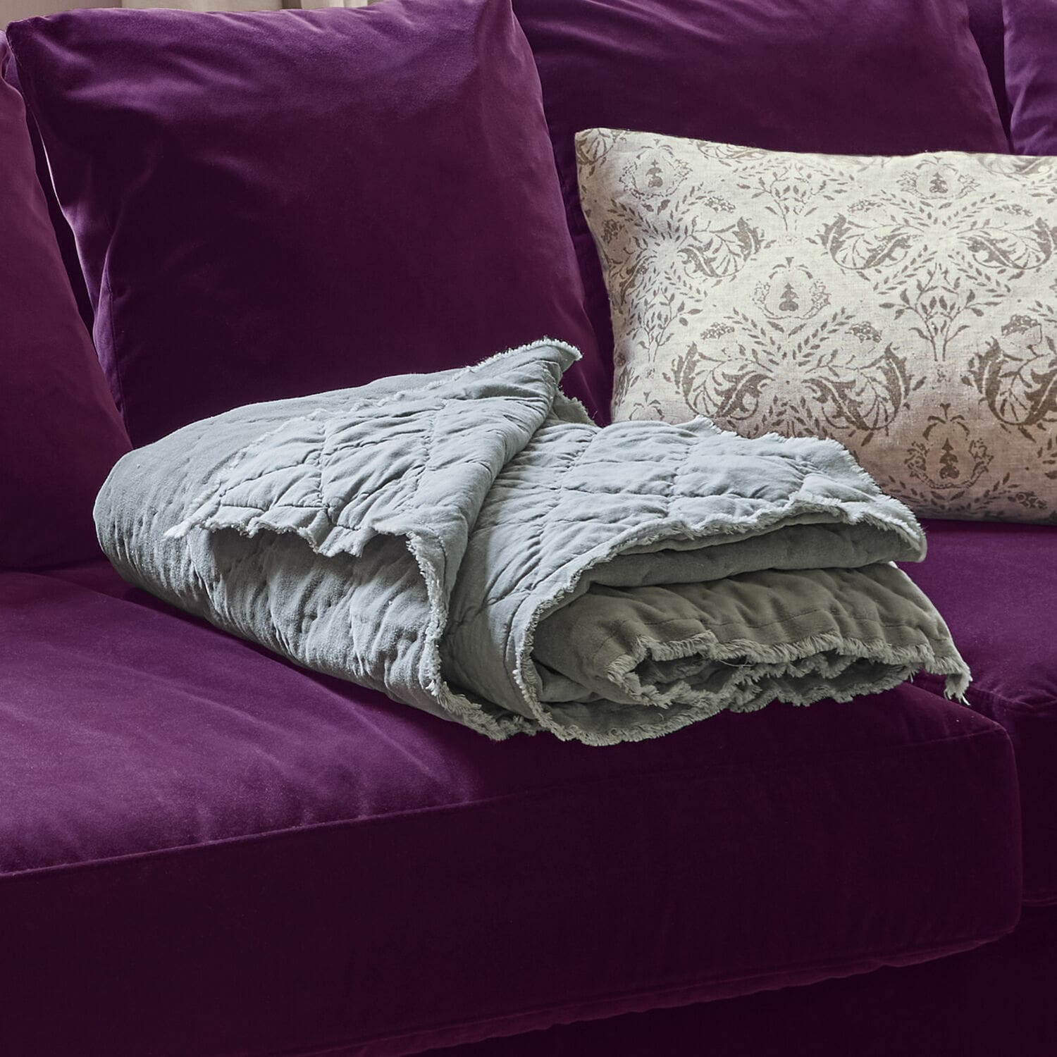 Grau gesteppte Baumwolldecke auf violettem Sofa mit dekorativem Kissen, Wohntextilien