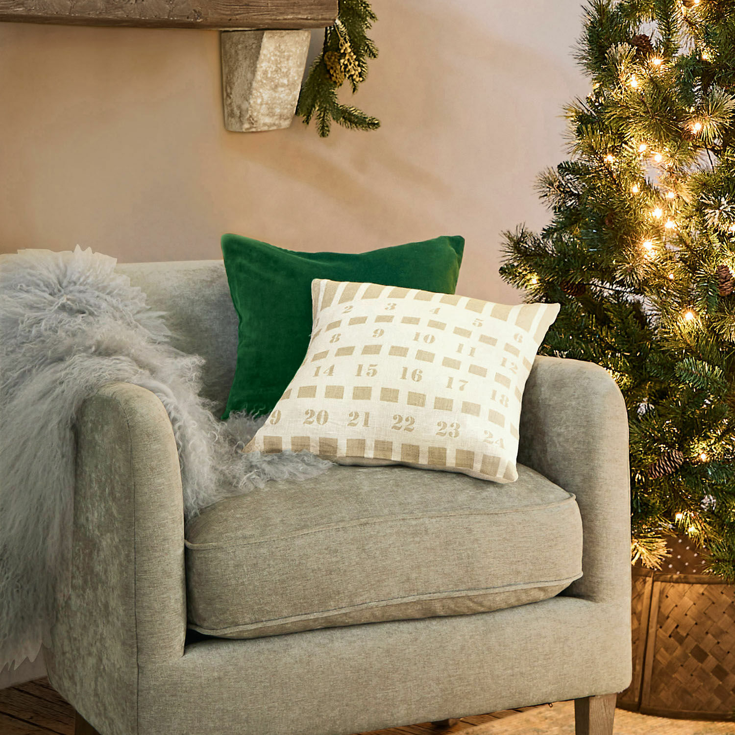 Grau bezogener Sessel mit grünem und beigem Kissen neben beleuchtetem Weihnachtsbaum im Wohnzimmer