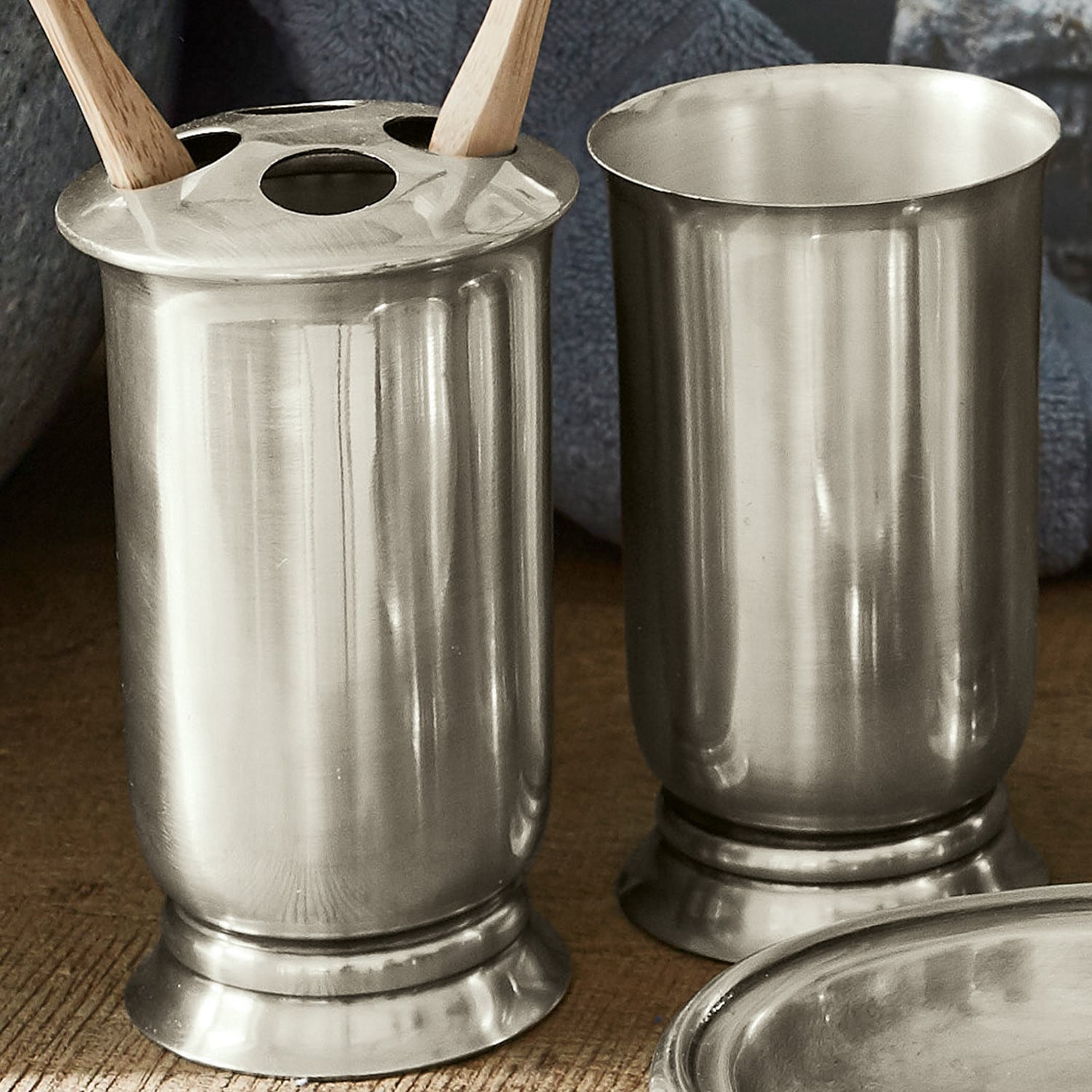 Zwei silberne Metallbecher auf Holztisch, einer mit Löchern für Küchenutensilien