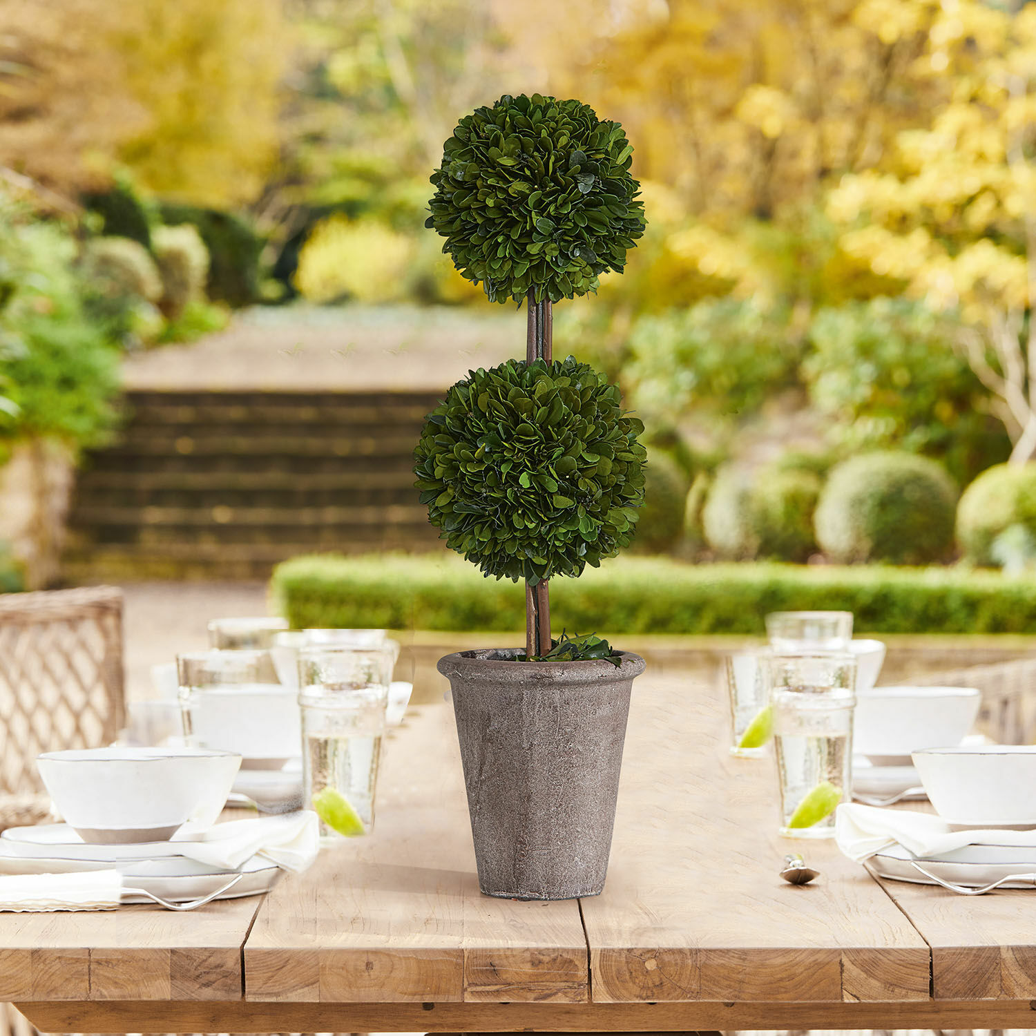 Künstliche Zierpflanze in grauem Steintopf auf Holztisch im Garten