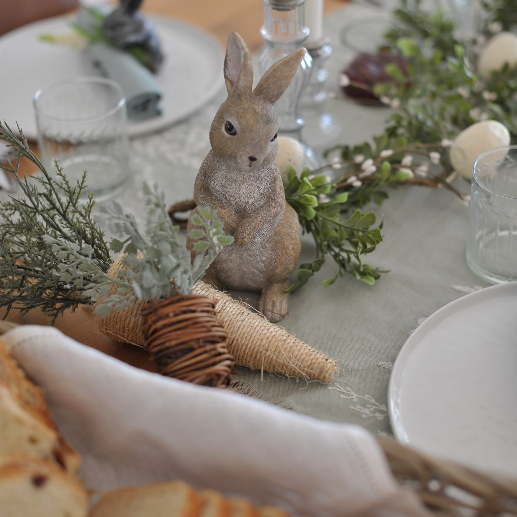 Dekorativer Hase auf Tisch mit natürlichen Deko-Elementen und Glas, Frühlingsdeko