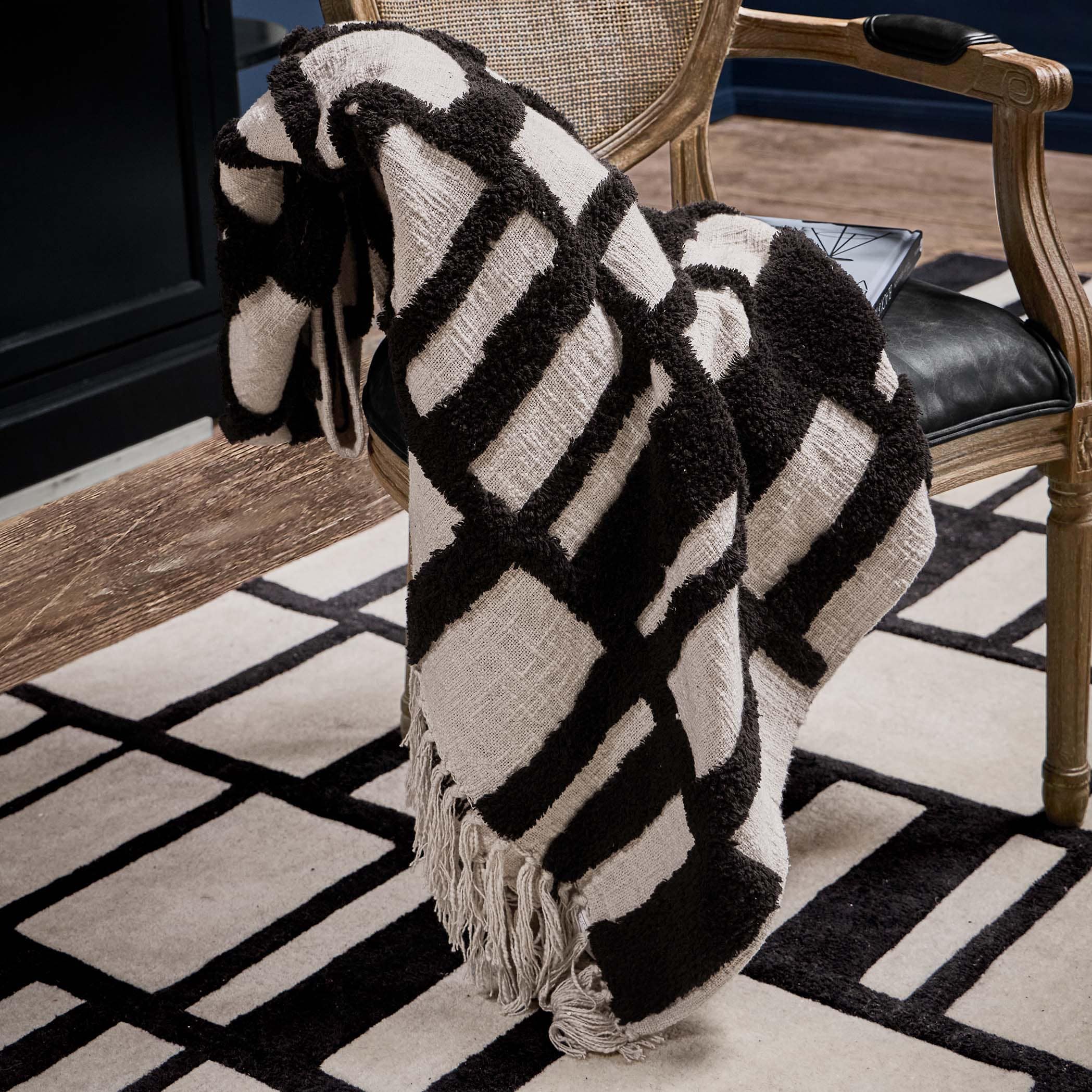 Schwarz-weißes Plaid mit geometrischem Muster aus weichem Stoff auf Holzstuhl im Wohnzimmer